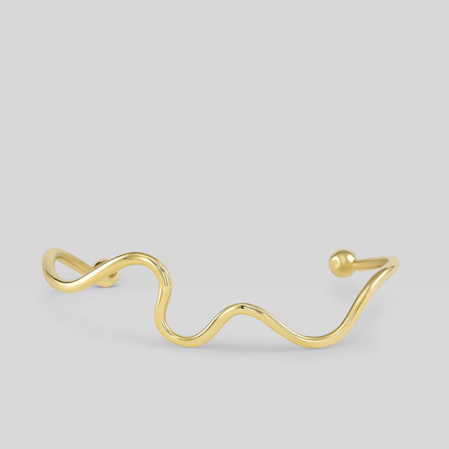 Gold wave-shaped bracelet on a light gray background