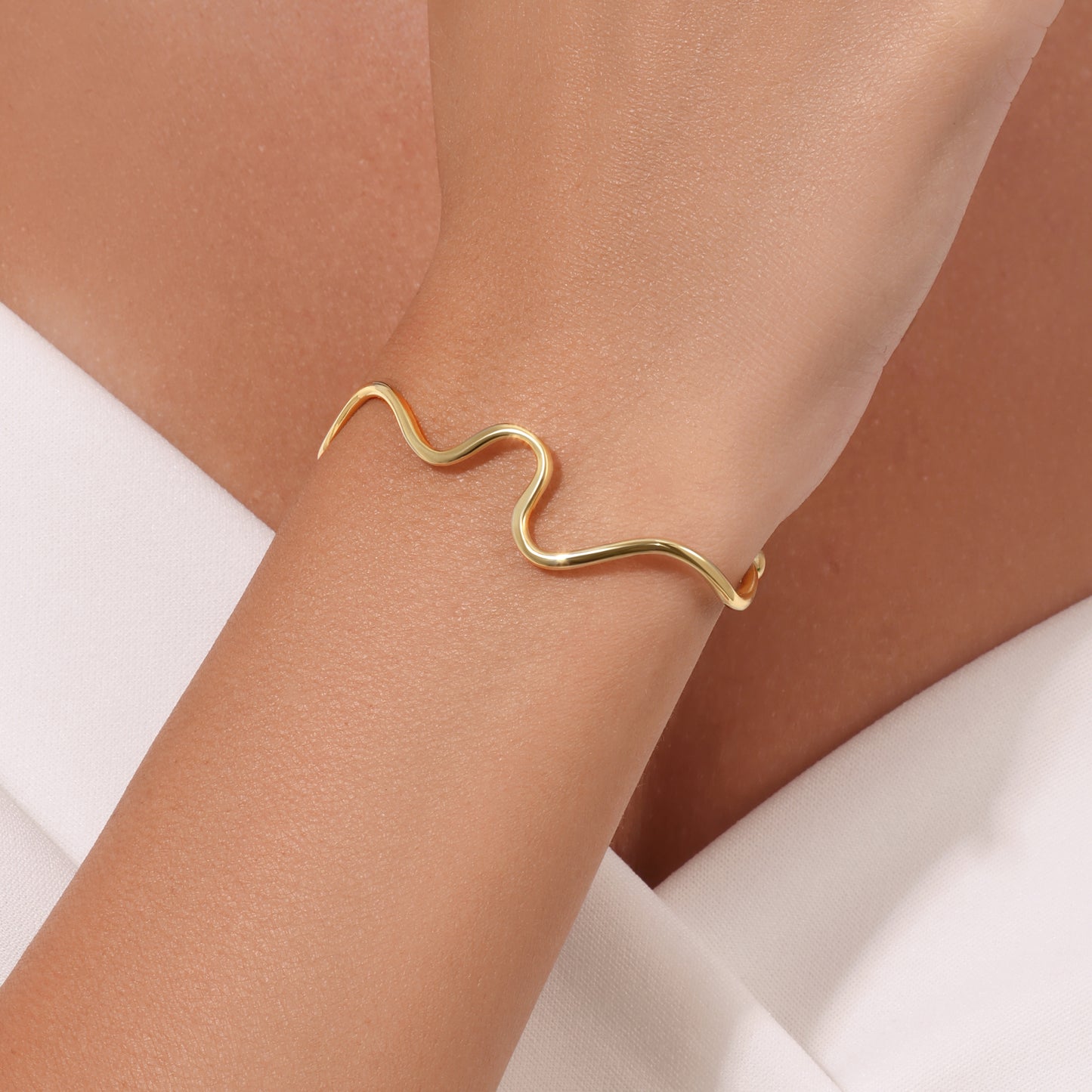 Gold wave-shaped bracelet on a wrist with a neutral background