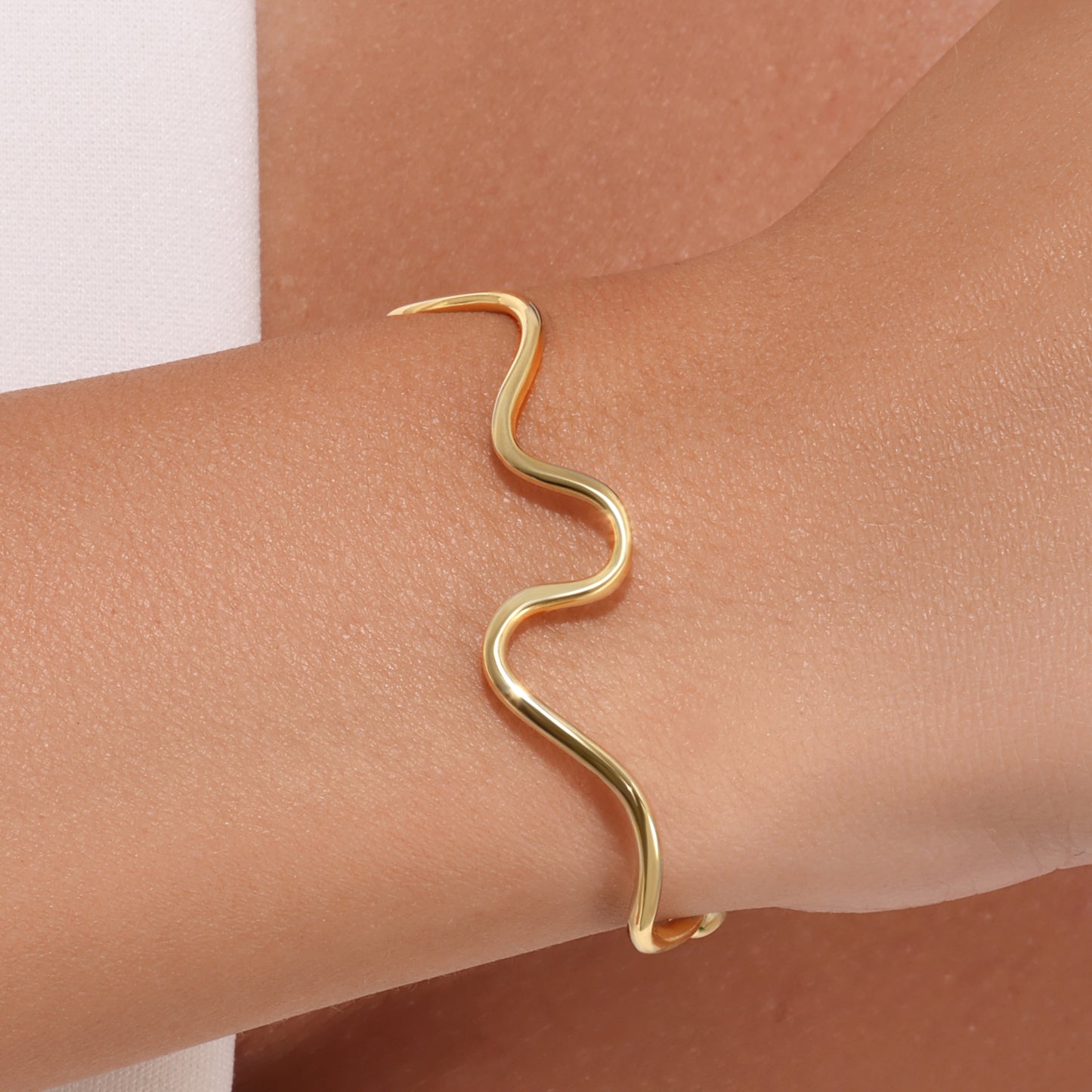 Gold wave-shaped bracelet on a wrist against a neutral background