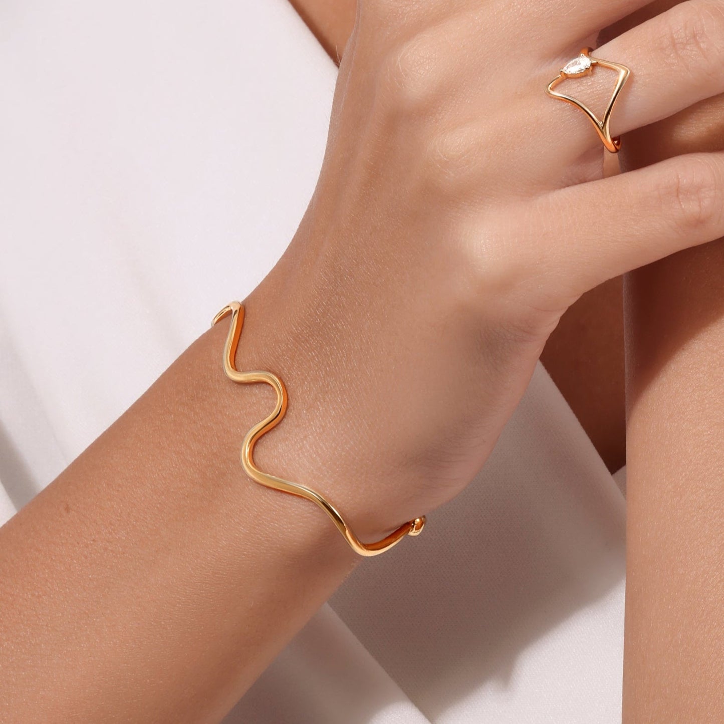 Gold bracelet and ring on a hand against a neutral background