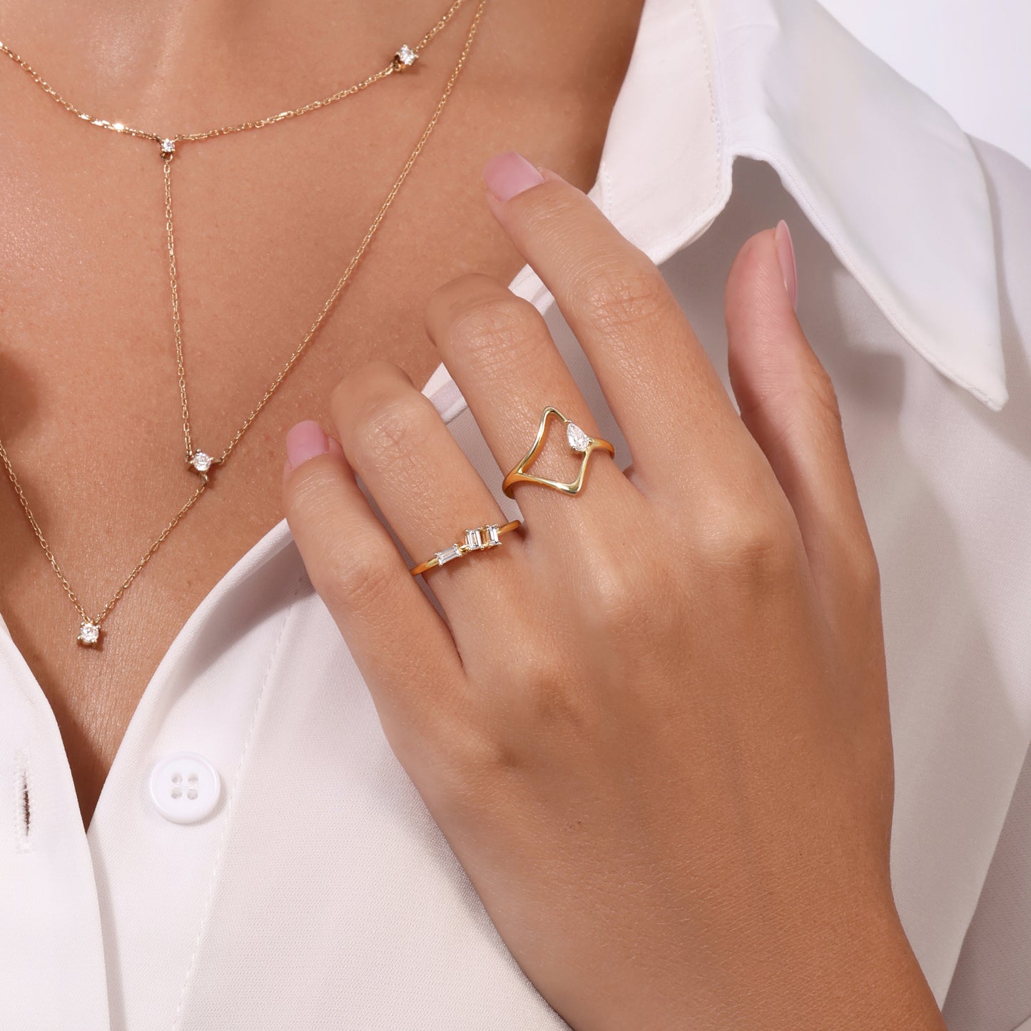 Gold wave ring with pear diamond, baguette diamond band ring, and delicate gold necklace with small diamond pendant