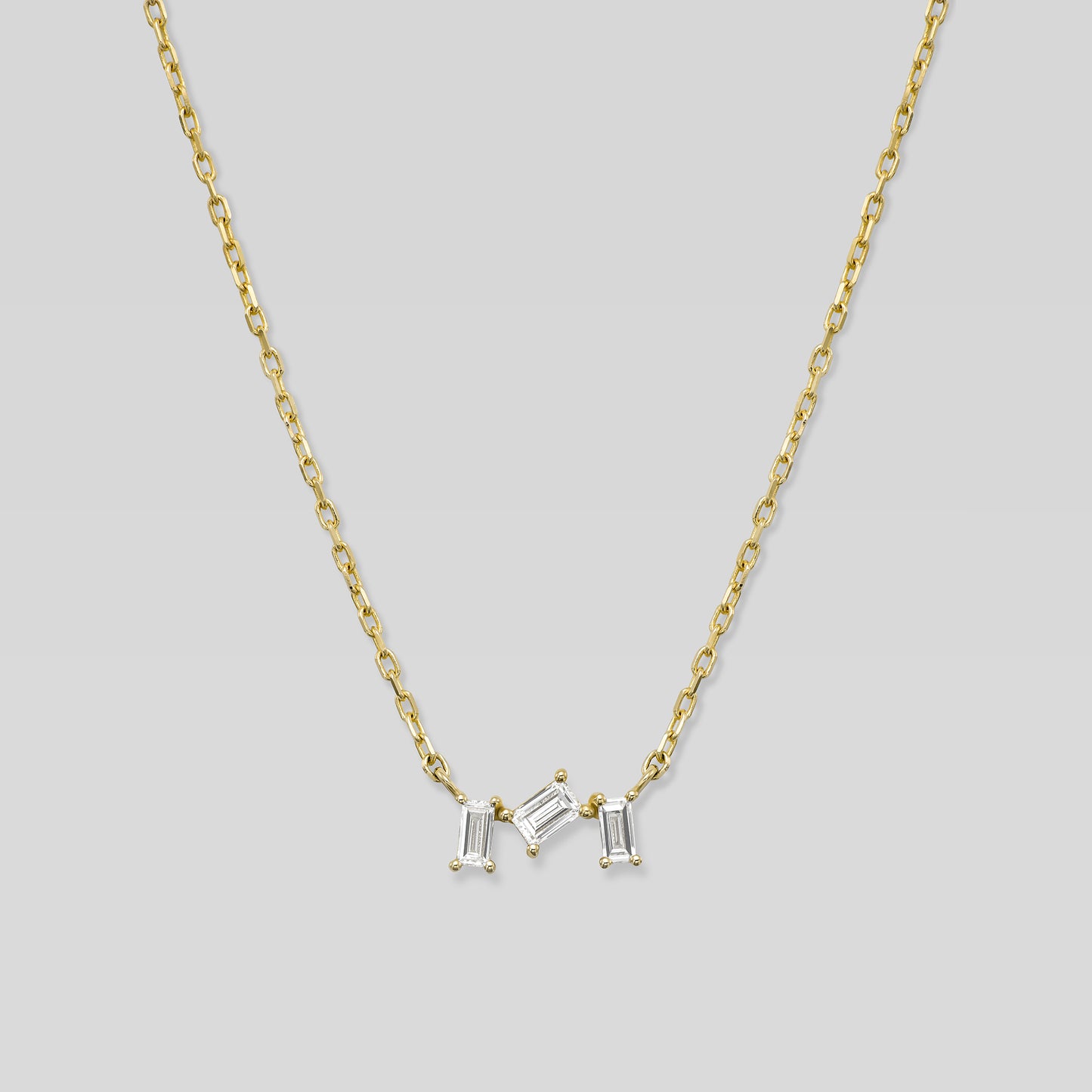 Gold necklace with three baguette-shaped diamonds on a light gray background