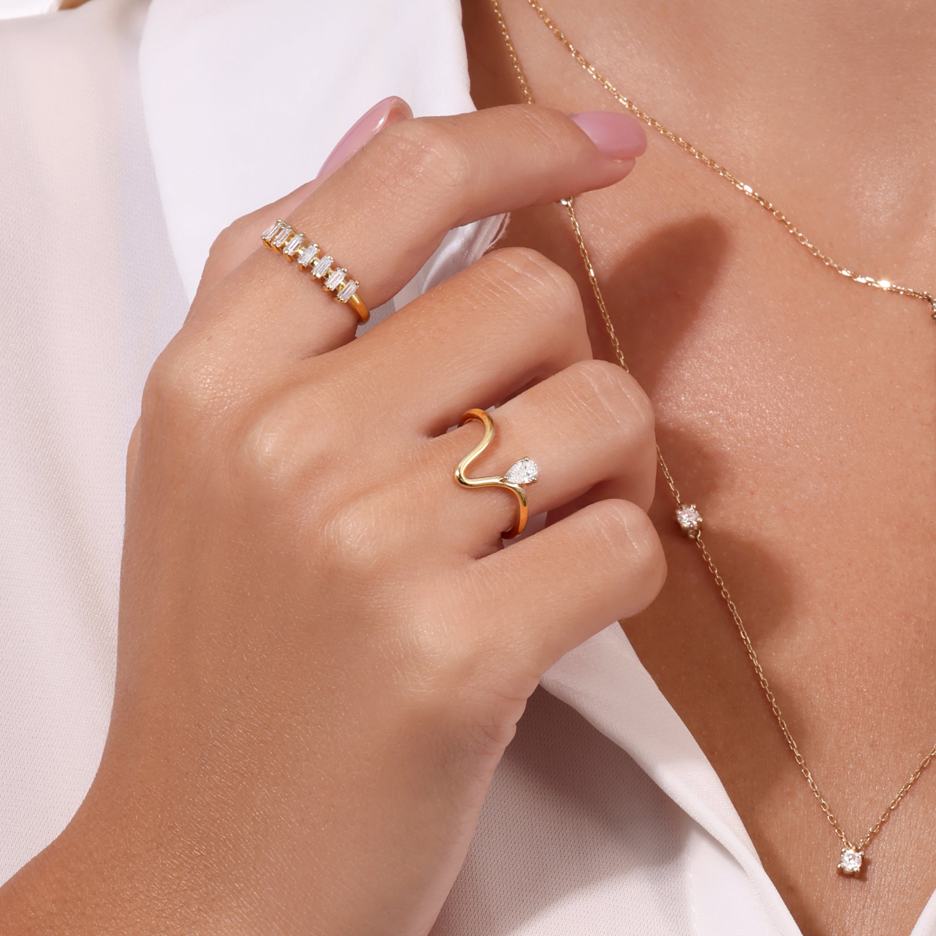Model wearing Levi Tzeiger Jewelry gold rings with diamond details, matching gold bracelet and hoop earrings, styled in an elegant white off-shoulder outfit