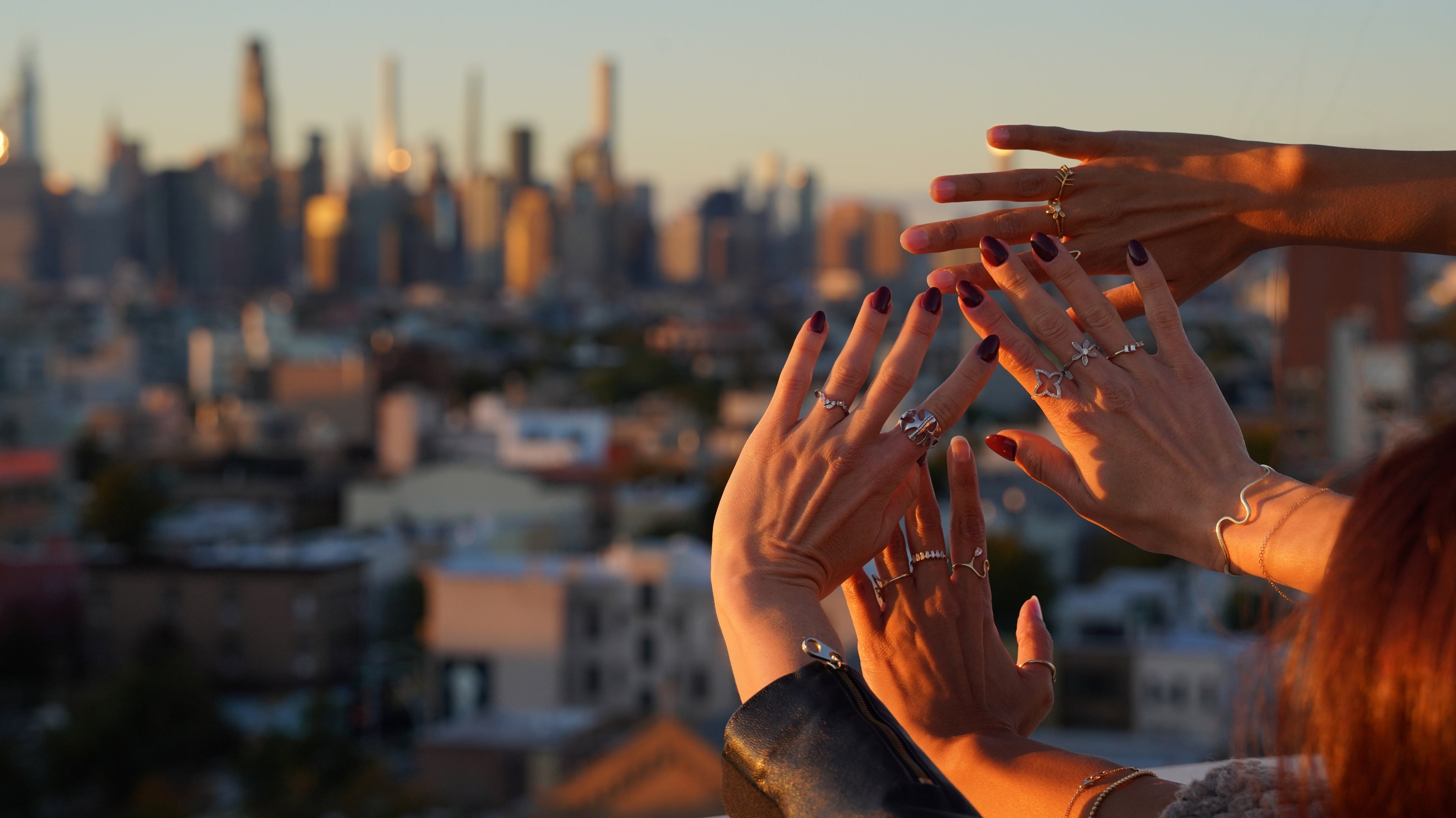Two pairs of hands reaching towards each other with a cityscape in the background during sunset.