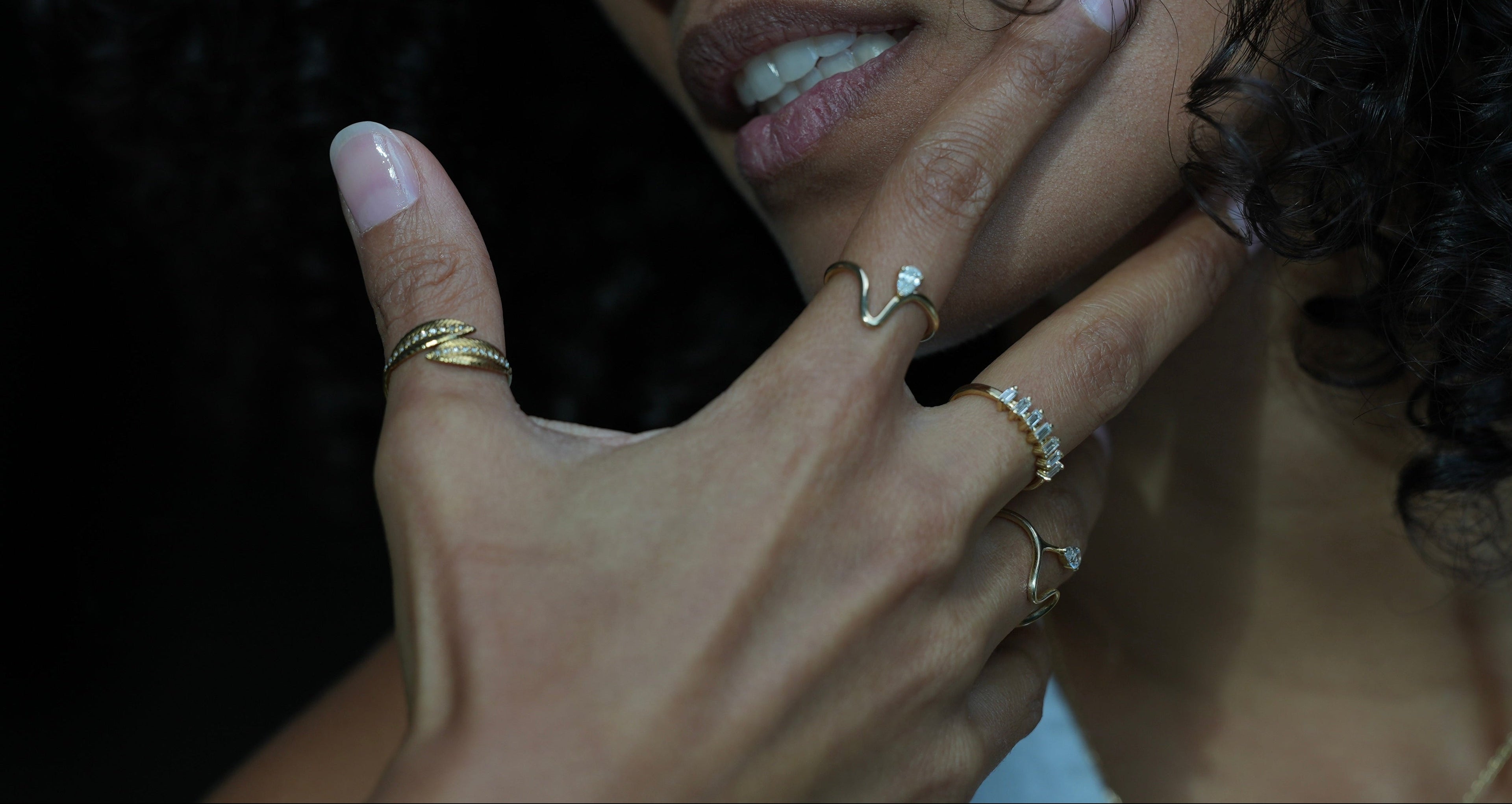 Close-up of a person's hand with multiple gold rings on a dark background