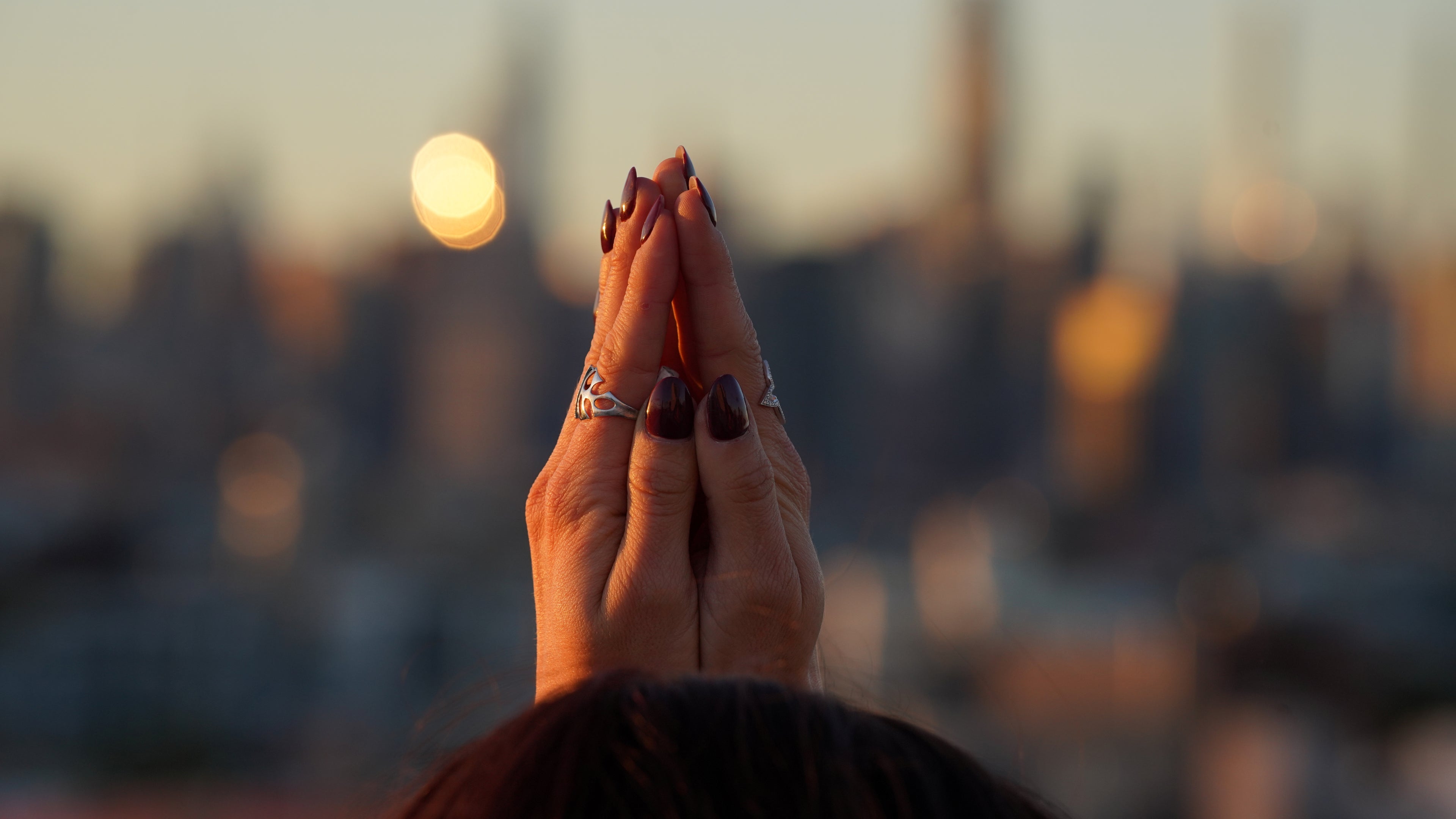 Hands holding a small object against a blurred cityscape at sunset