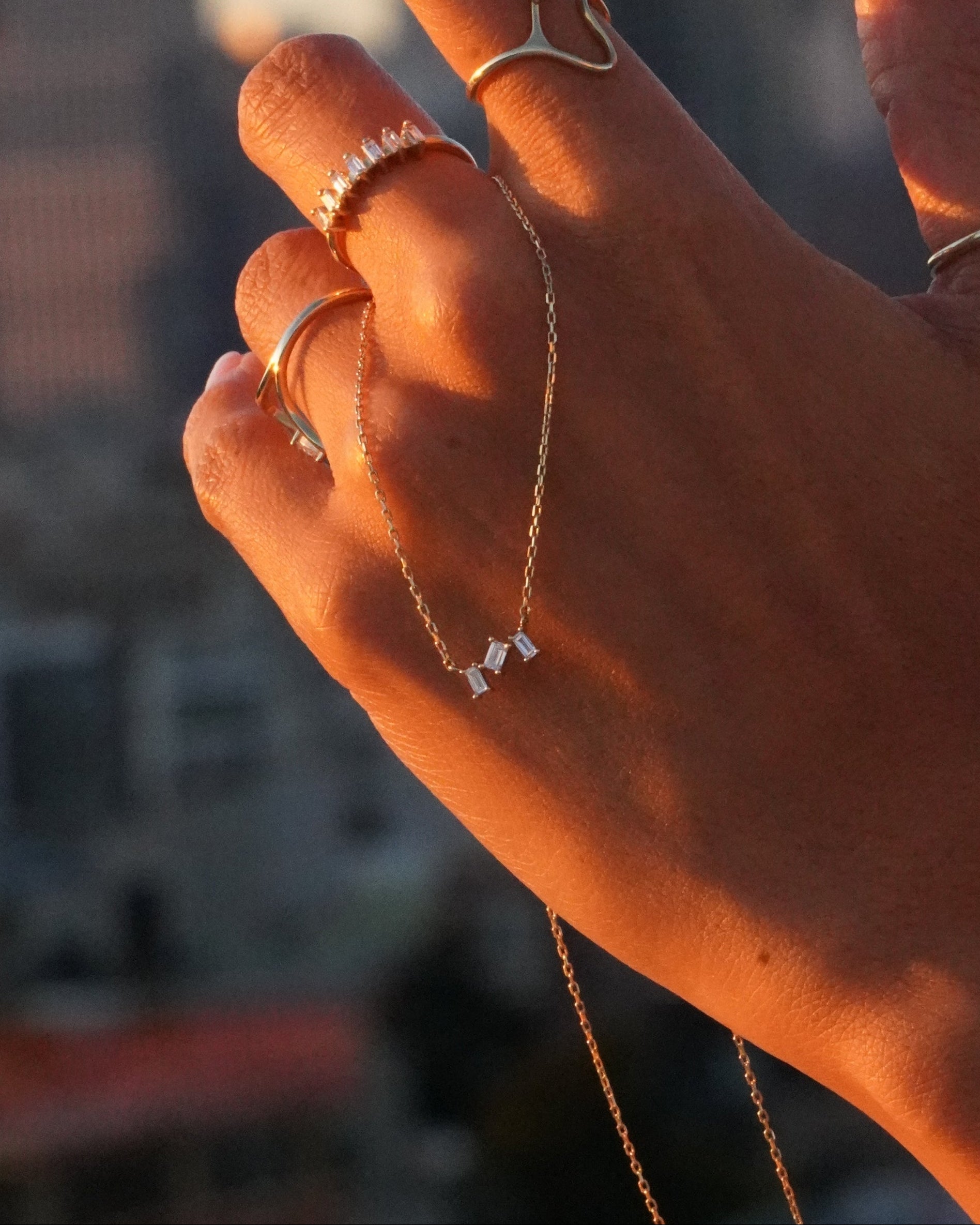 Hand with multiple rings holding a necklace against a blurred background