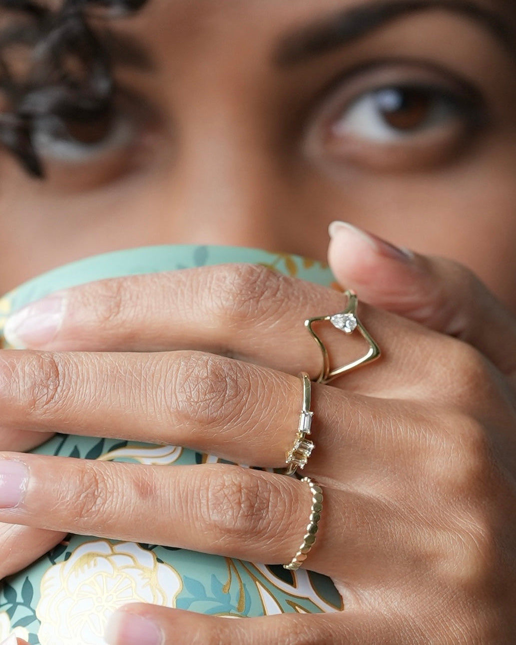 Close-up of a woman's hand with rings holding a cup, with a blurred background