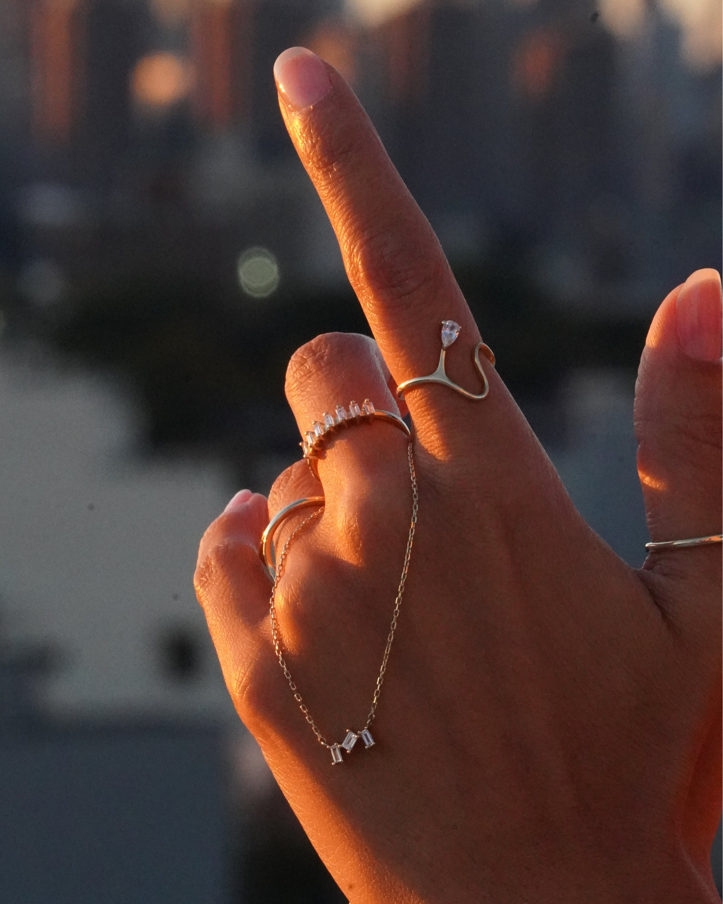 Hand with rings and a necklace against a blurred cityscape background