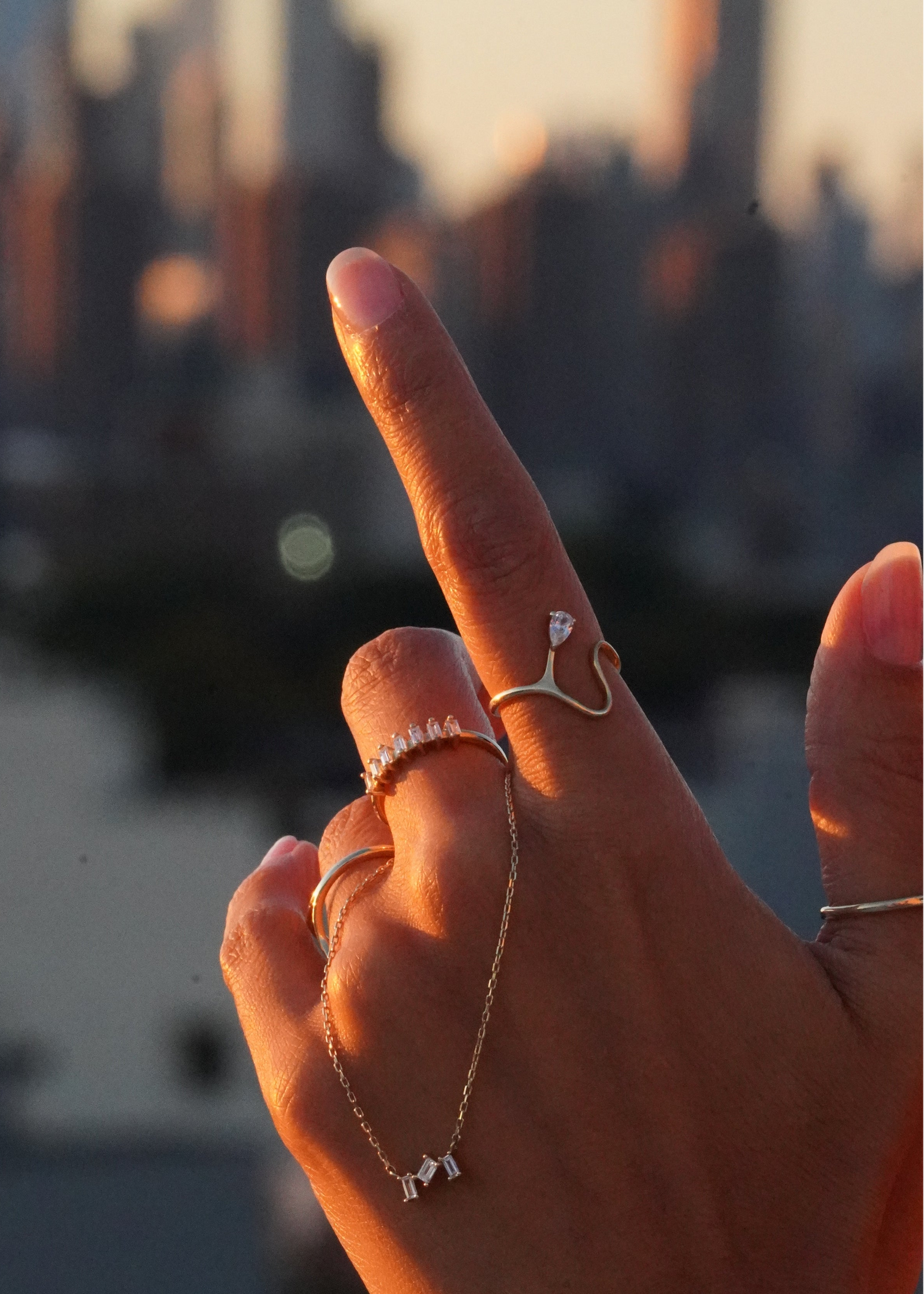 Hand with multiple rings and a necklace against a blurred cityscape background