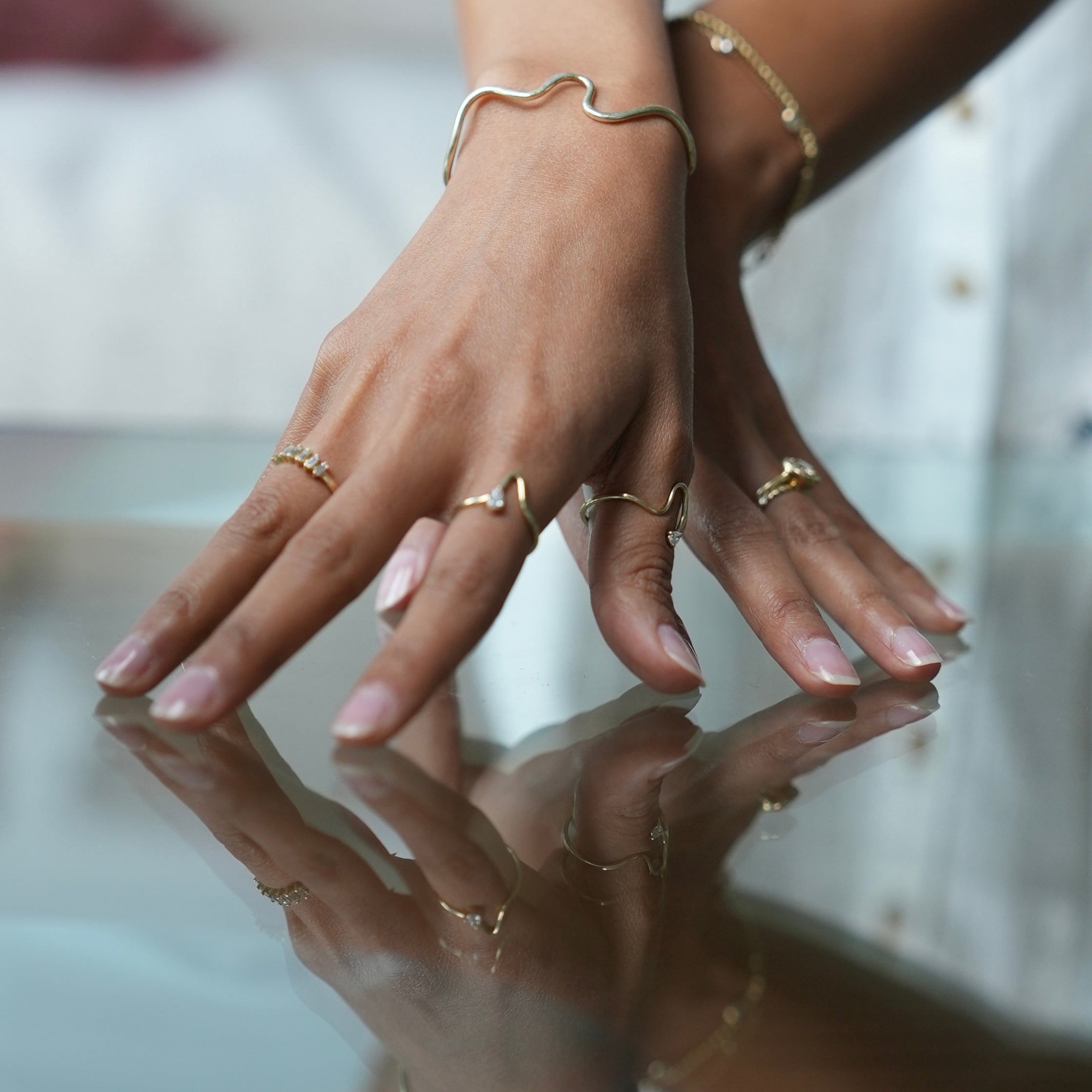 Close-up of hands with gold rings and bracelets on a reflective surface