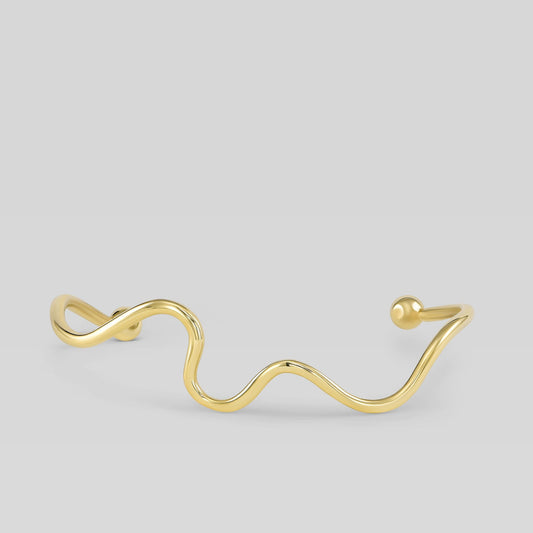 Gold wave-shaped bracelet on a light gray background