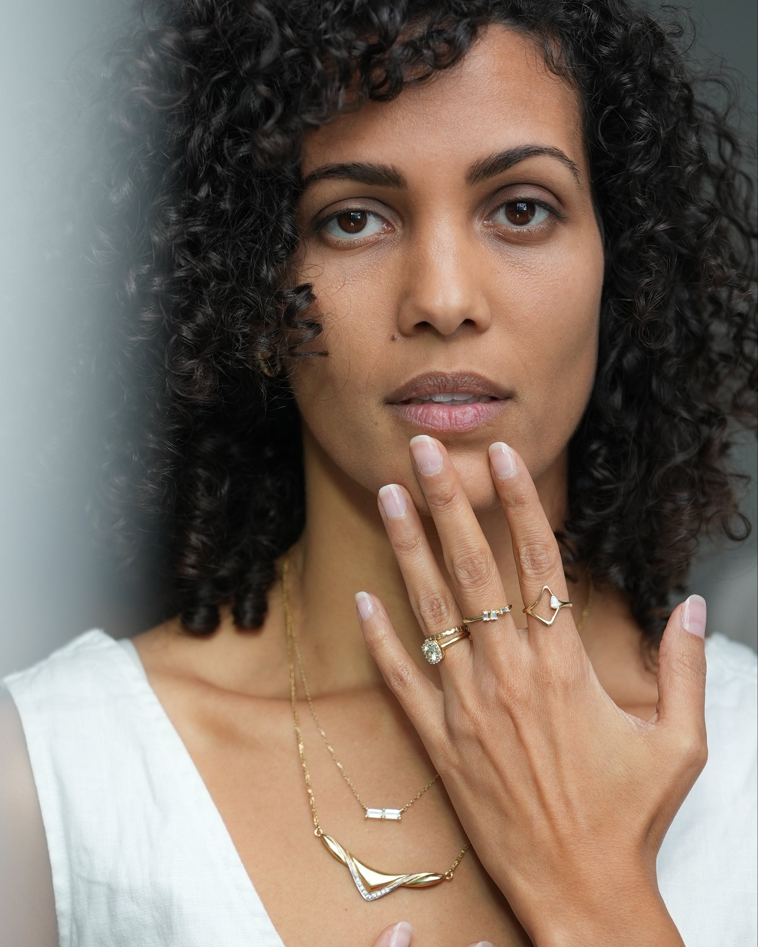 Woman with curly hair wearing a necklace and rings, against a neutral background