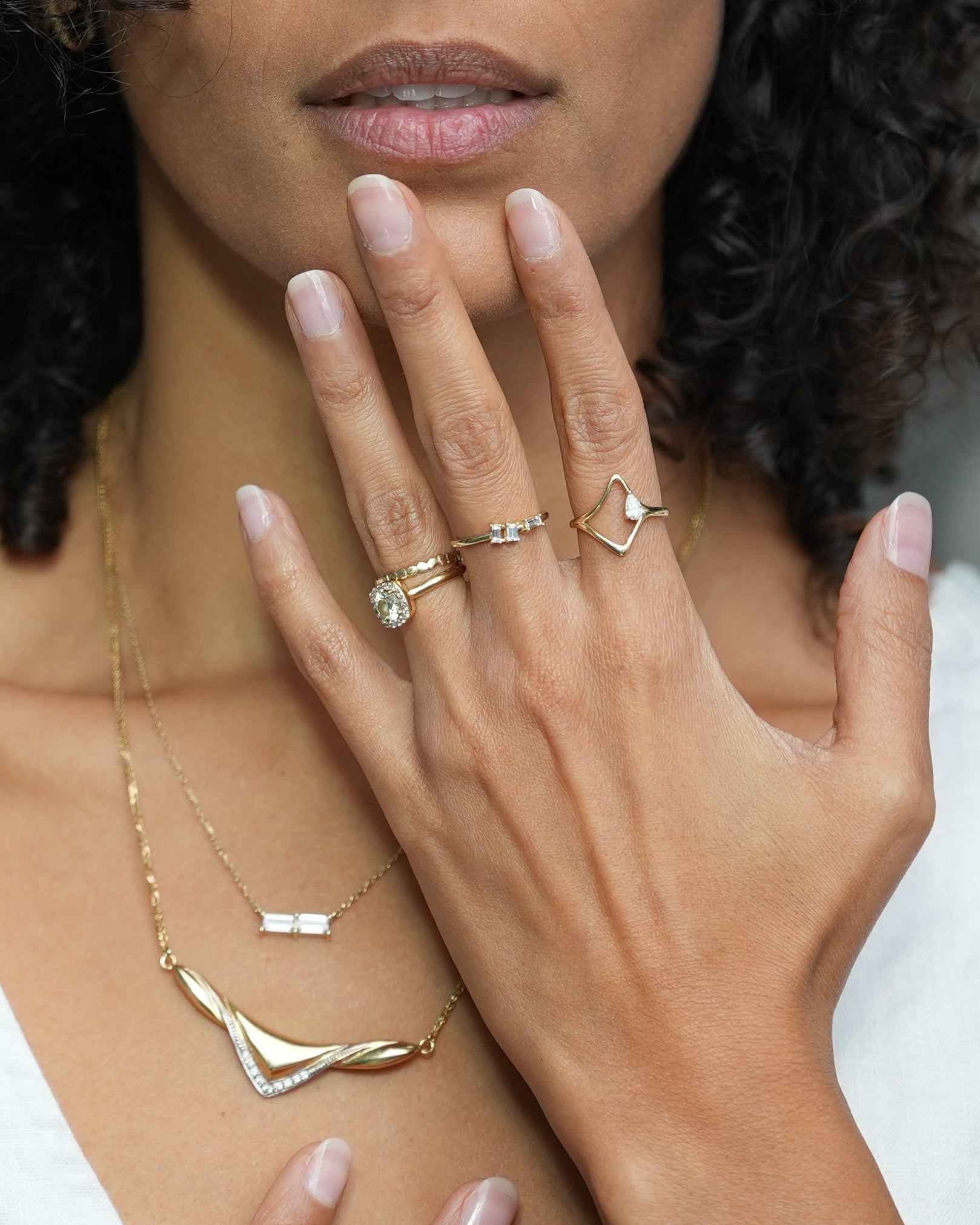 Woman with curly hair wearing jewelry, looking directly at the camera.