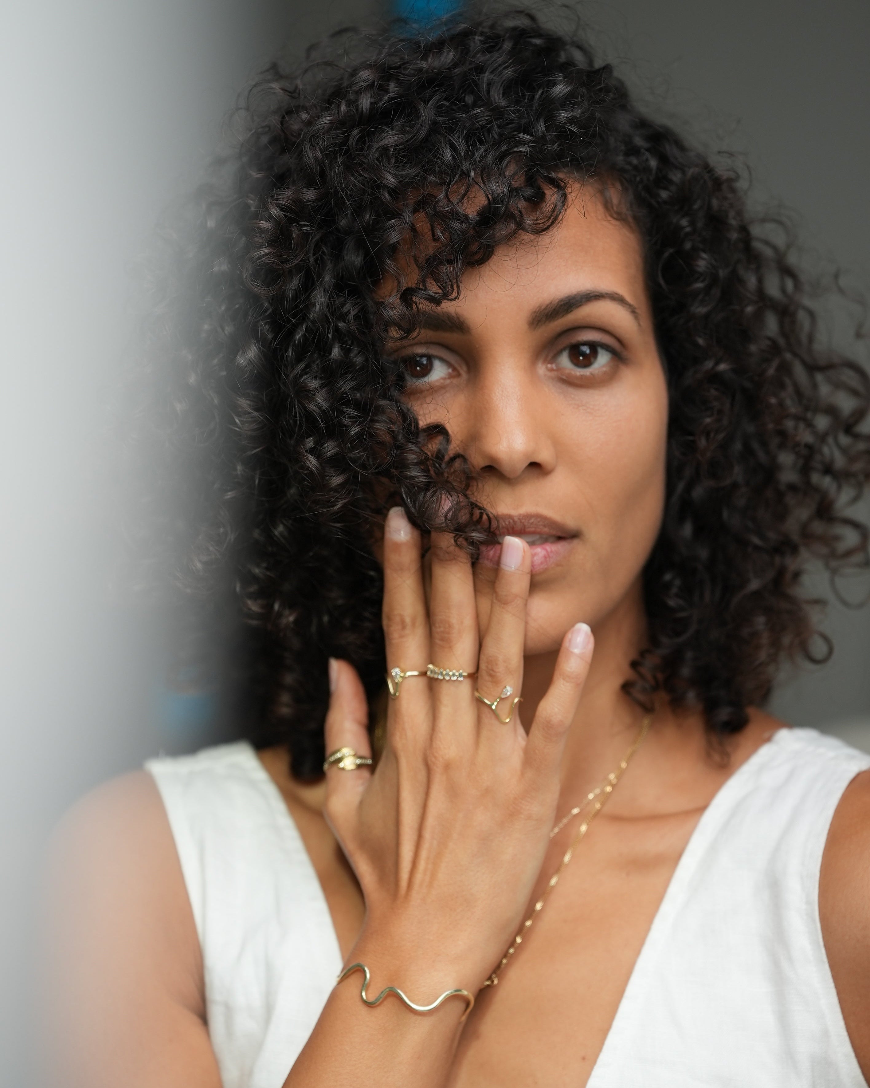 Woman with curly hair wearing a white top against a neutral background
