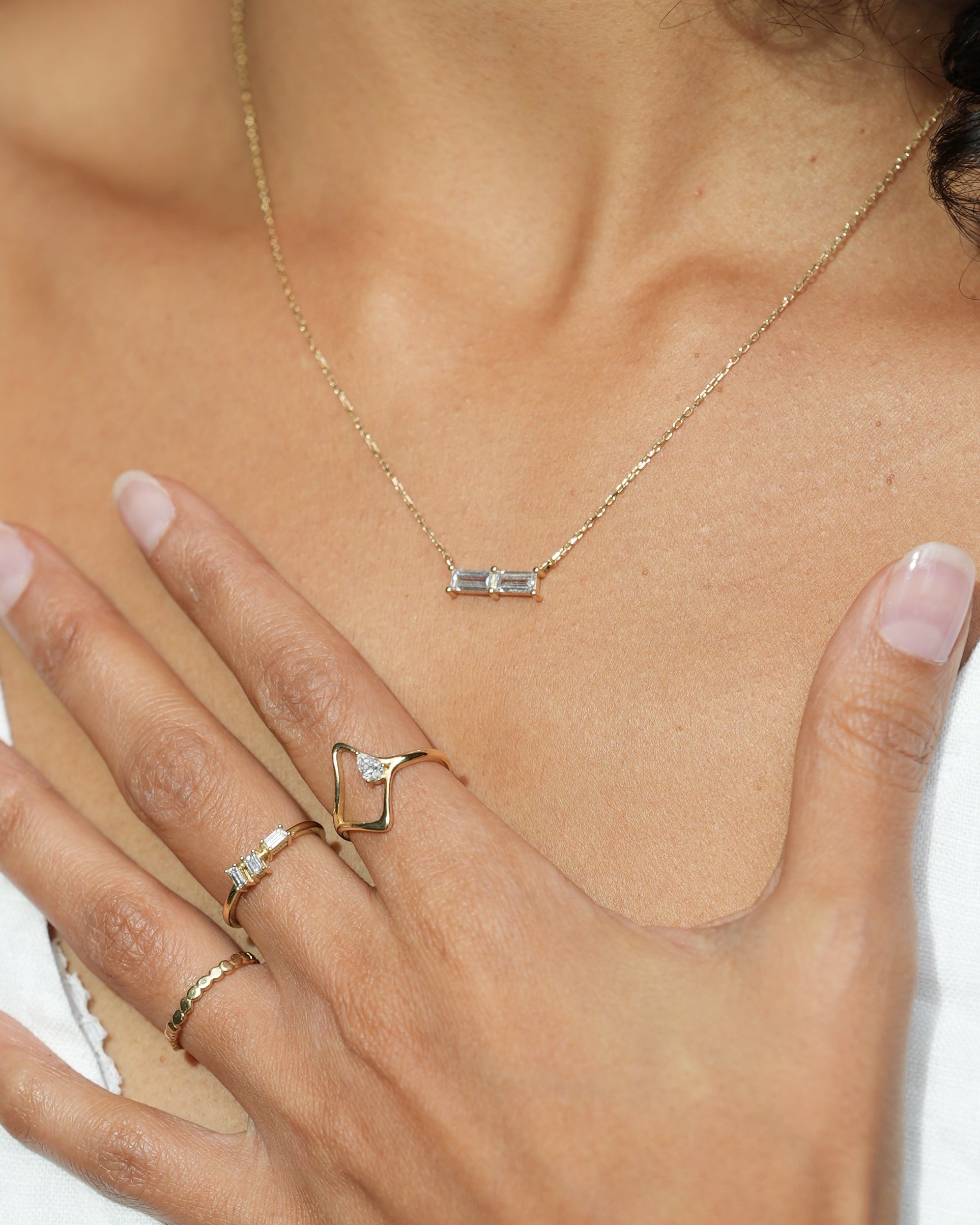 Close-up of a person wearing gold necklaces and rings with a white garment.