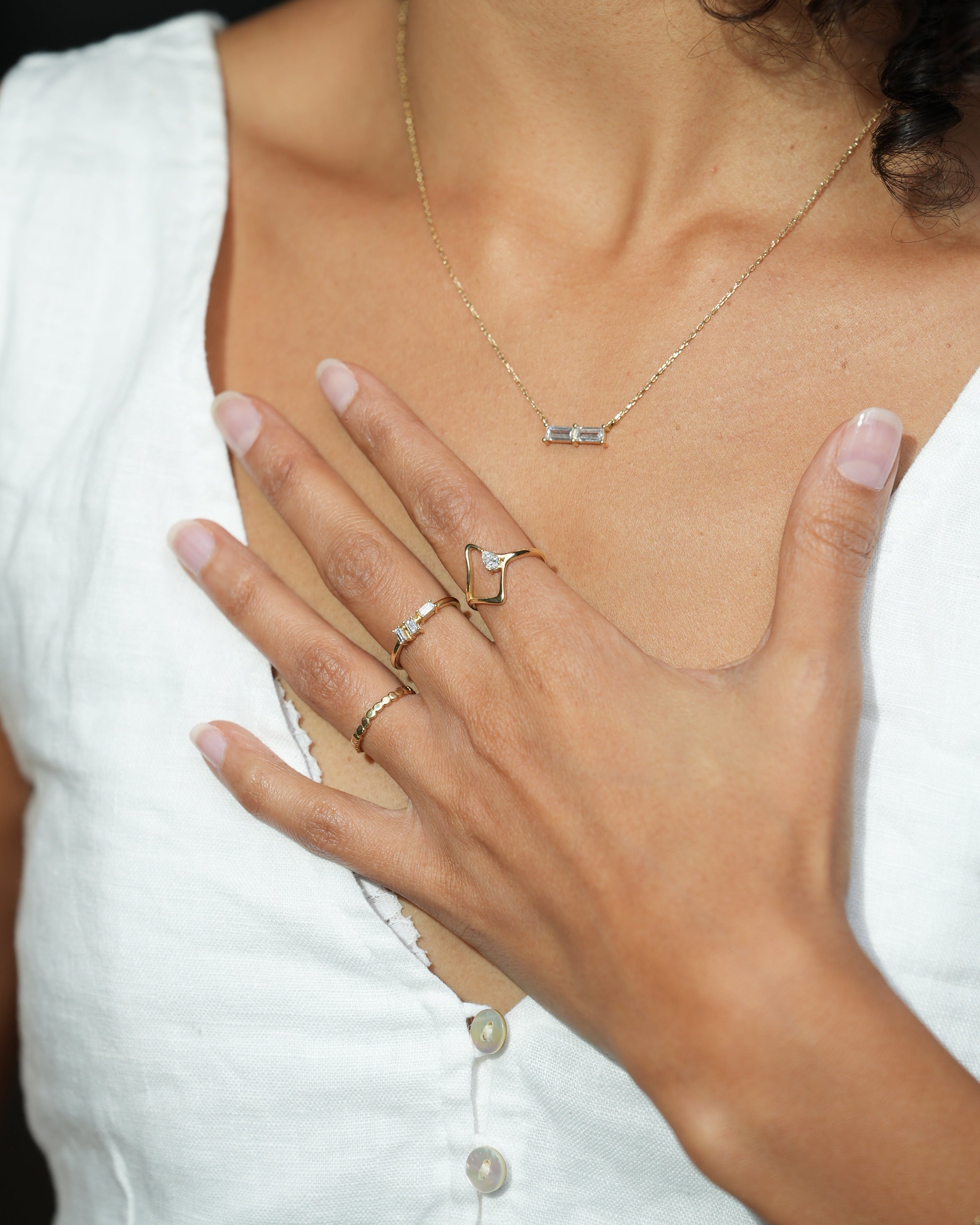 Close-up of a person wearing gold necklaces and rings with a white garment.
