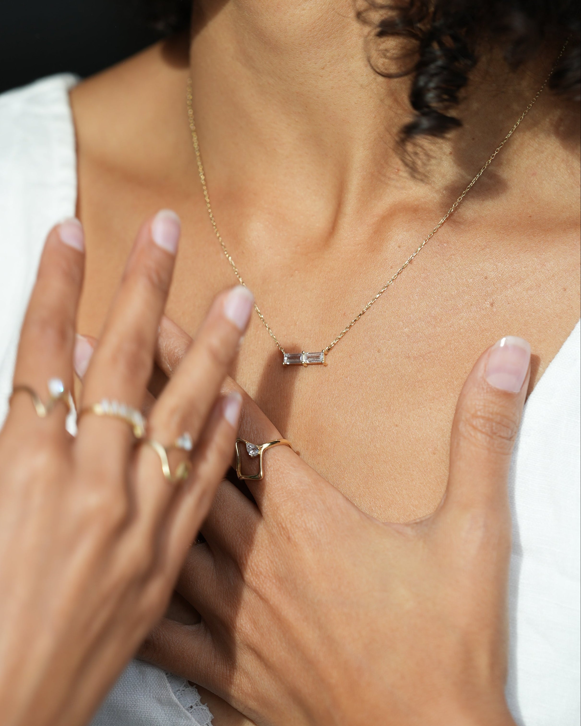 Close-up of a person's chest with jewelry and hands on a blurred background
