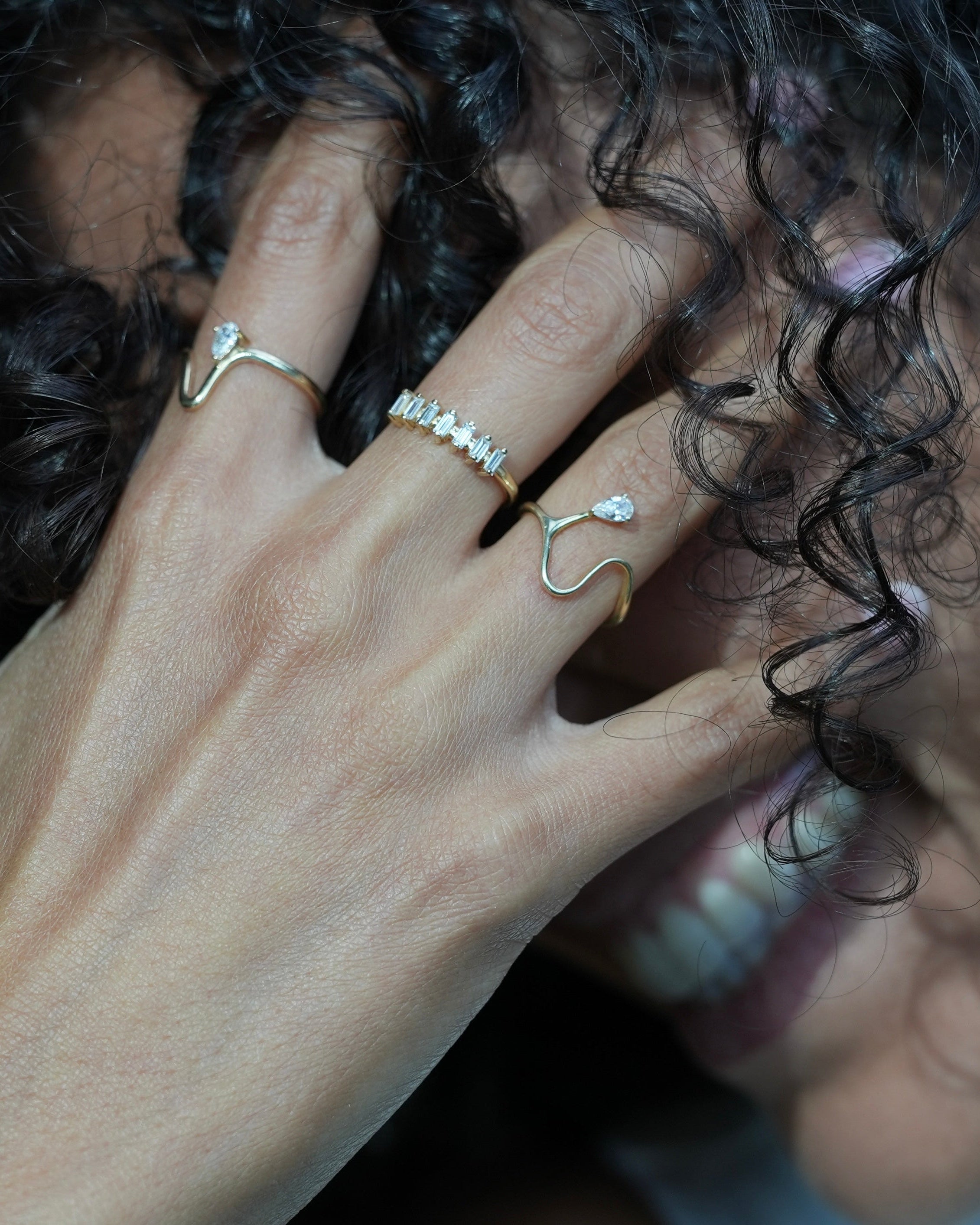 Close-up of a person's hand with rings on fingers, partially covering their face.