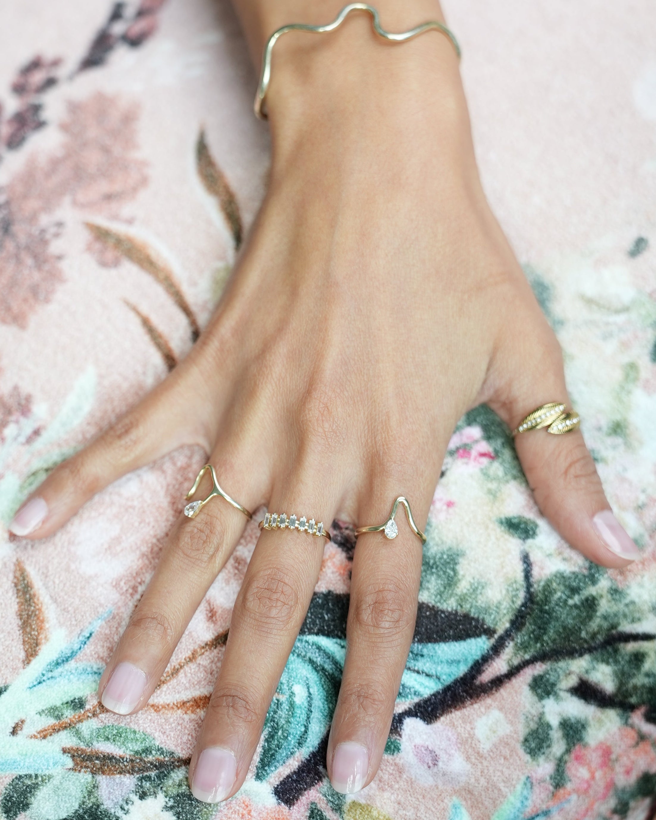 Close-up of a hand wearing multiple rings on a floral fabric background
