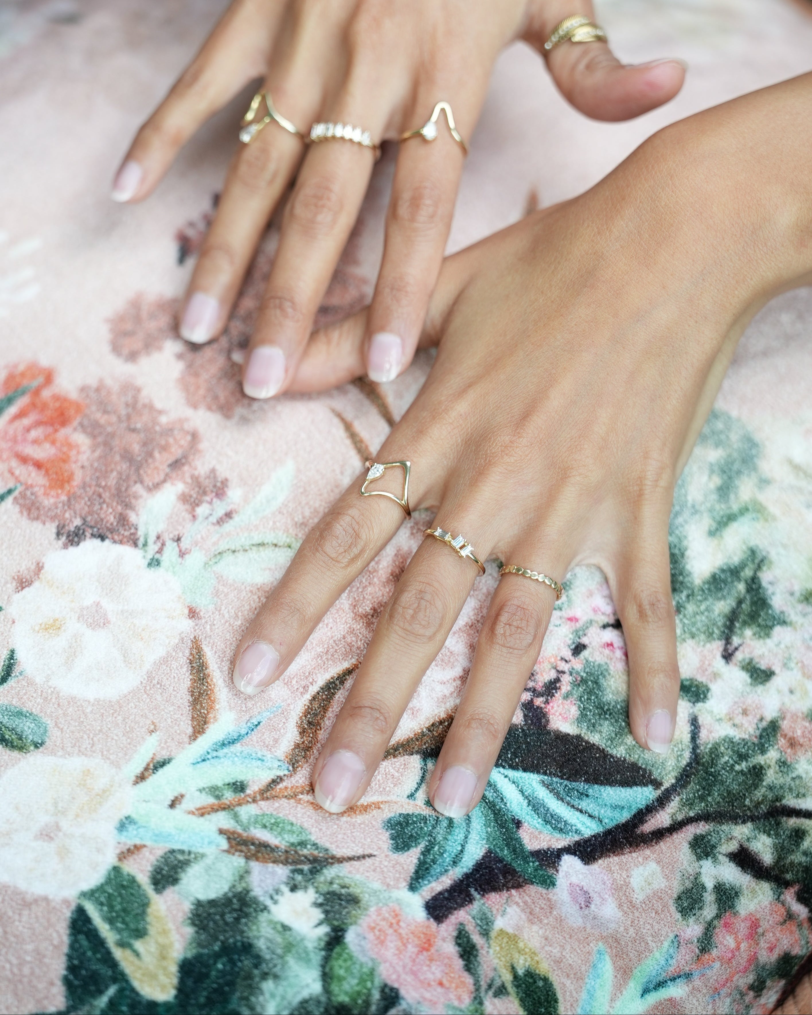 Close-up of hands with multiple rings on a floral fabric background
