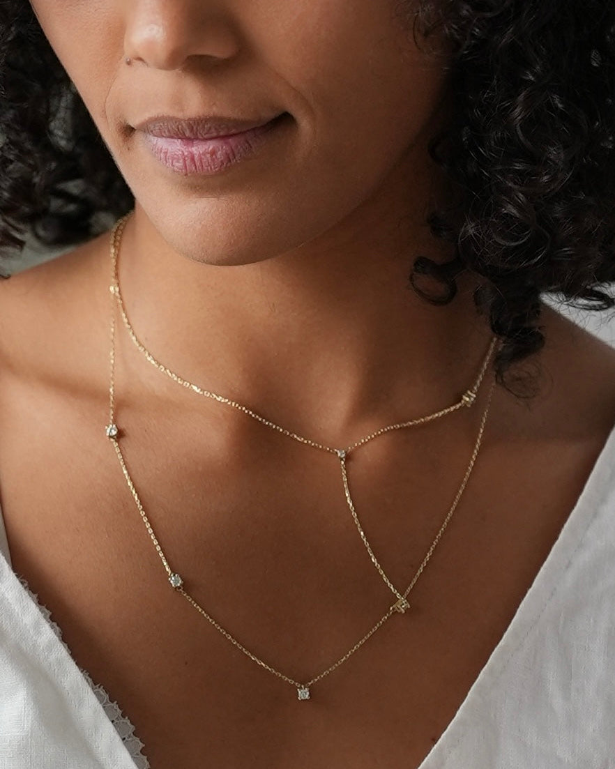 Woman wearing a delicate gold necklace with small stones, close-up of her neck and shoulders.