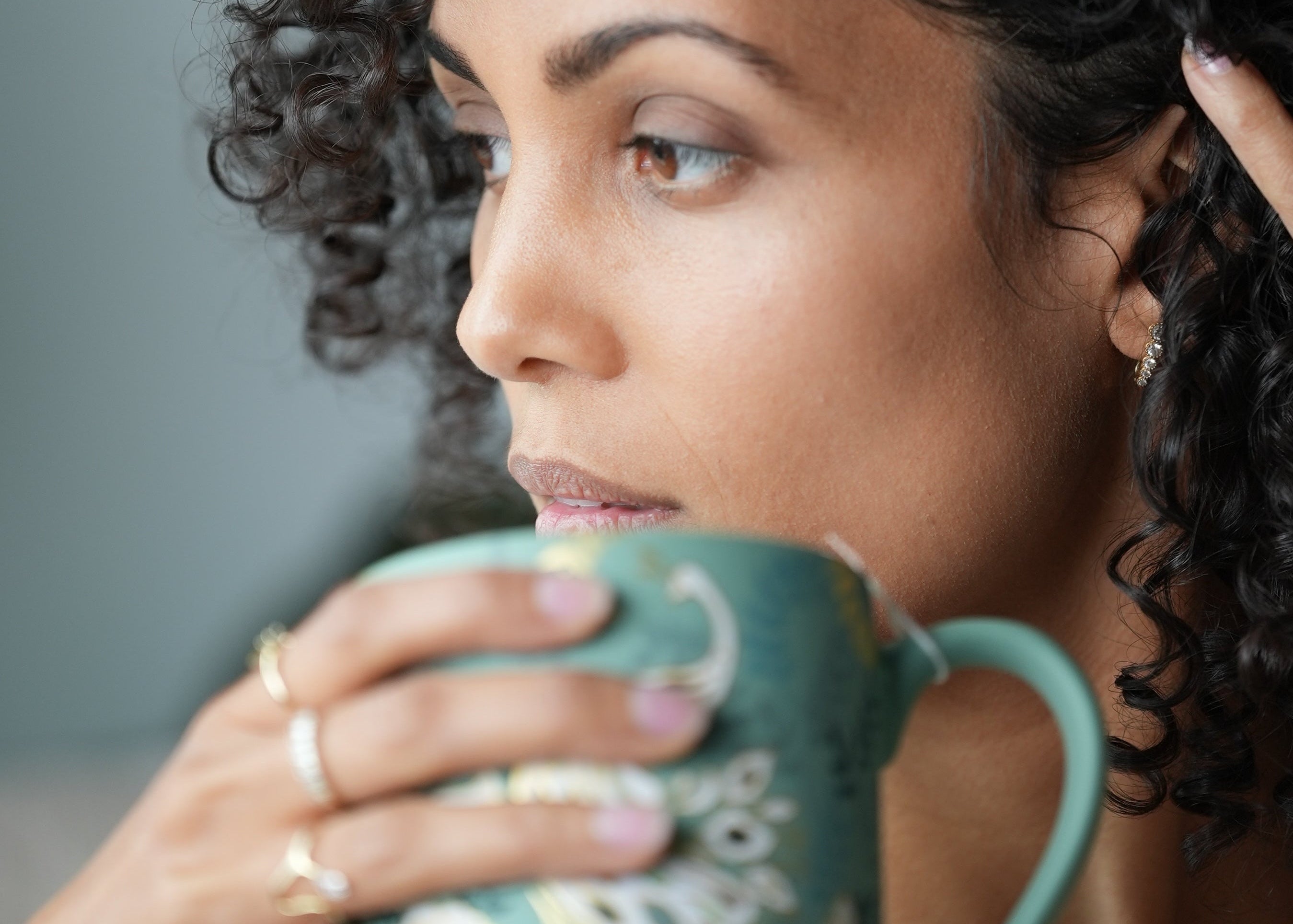 Woman drinking from a teal mug with a floral design against a neutral background