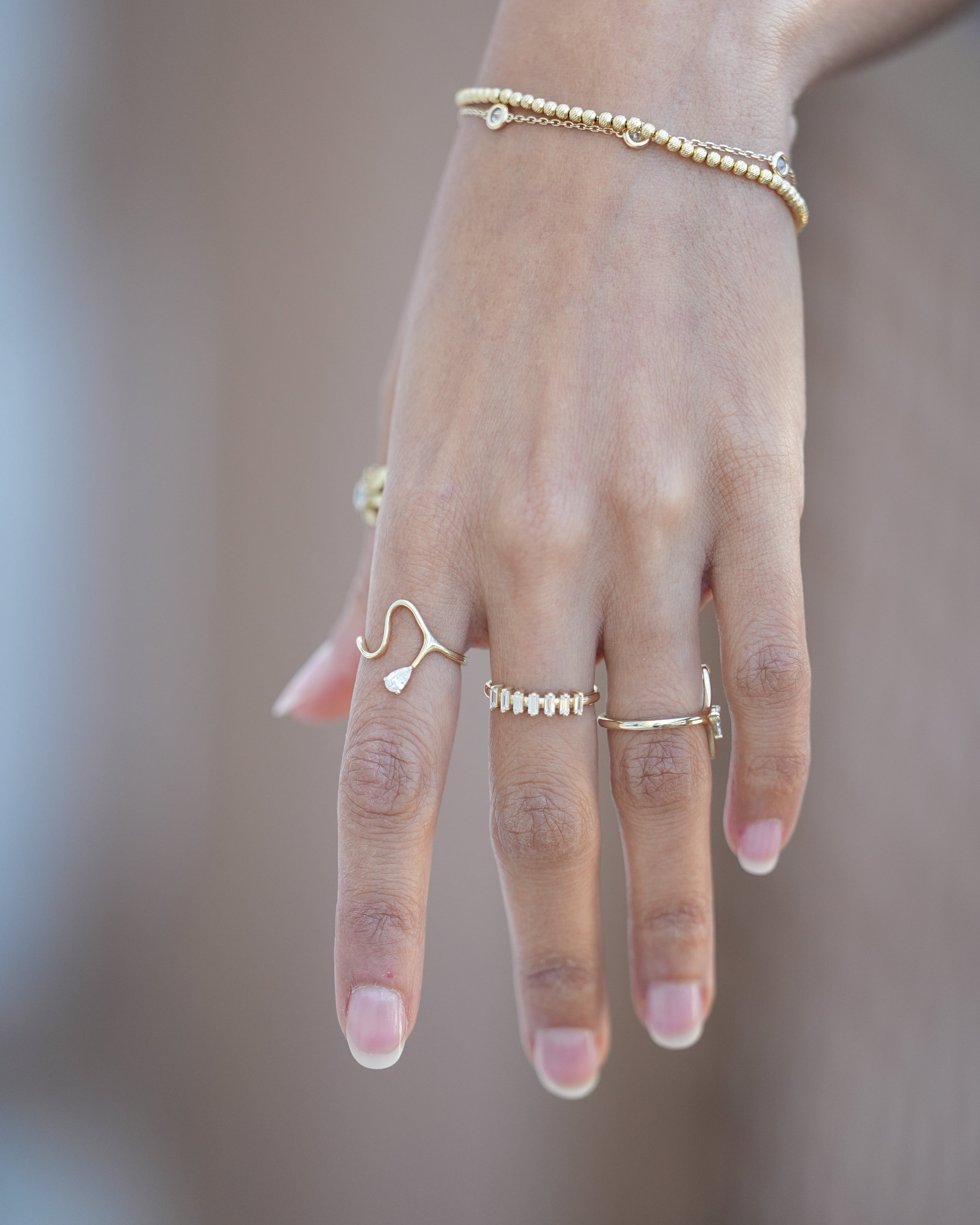 Hand wearing multiple gold rings and a bracelet on a blurred background