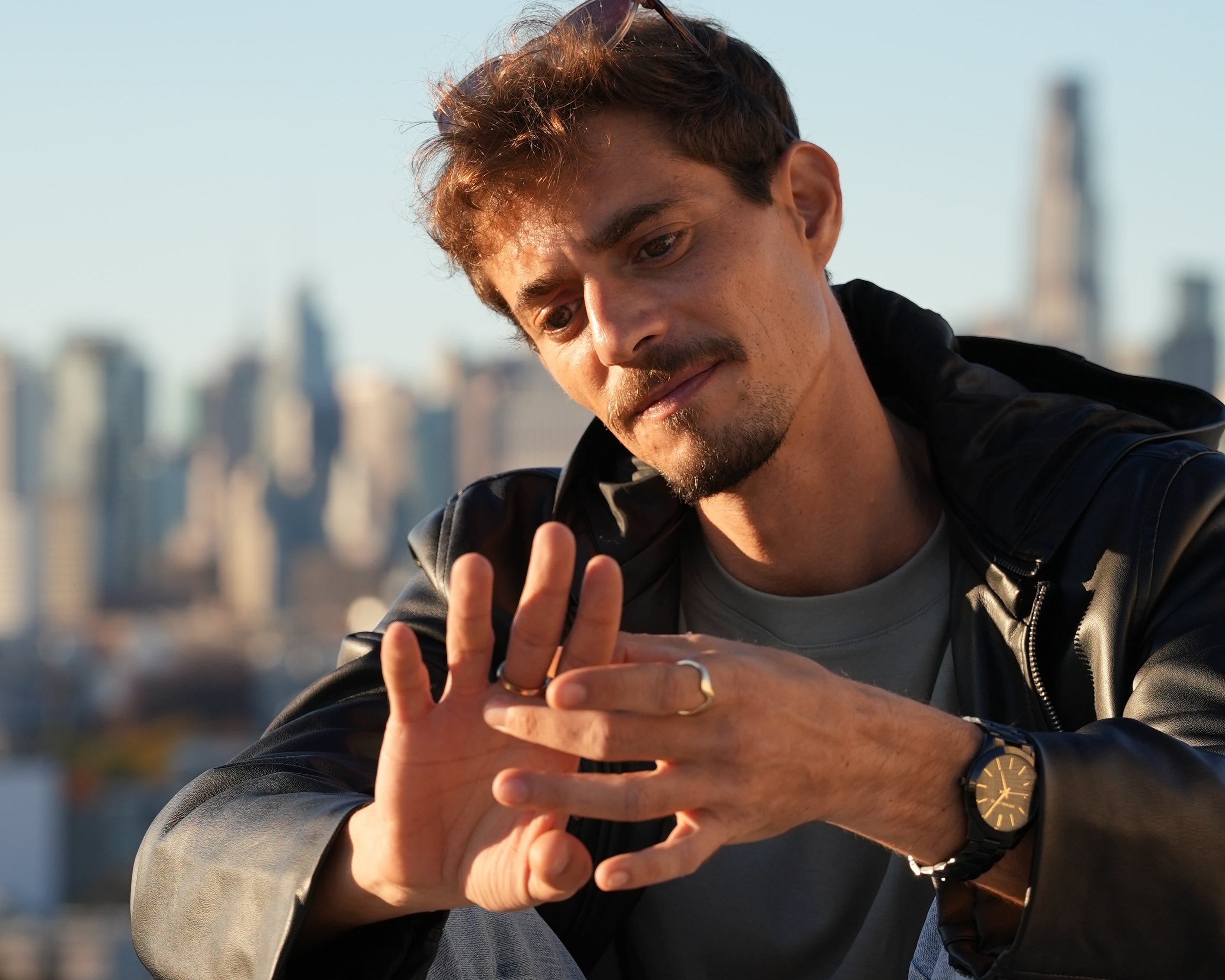 Man in a leather jacket and jeans sitting on a bench with a clear blue sky.