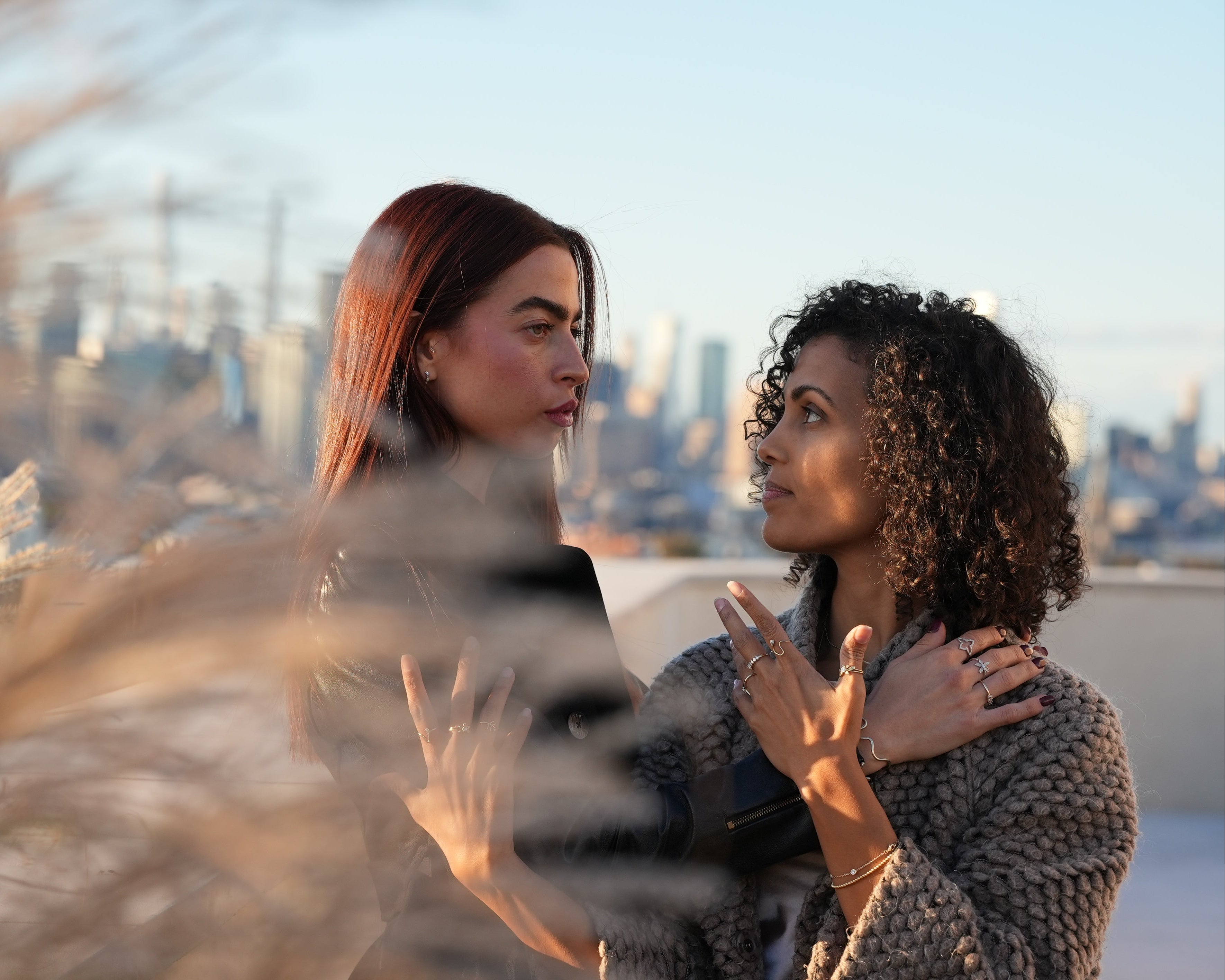 Two women embracing on a rooftop with a cityscape in the background