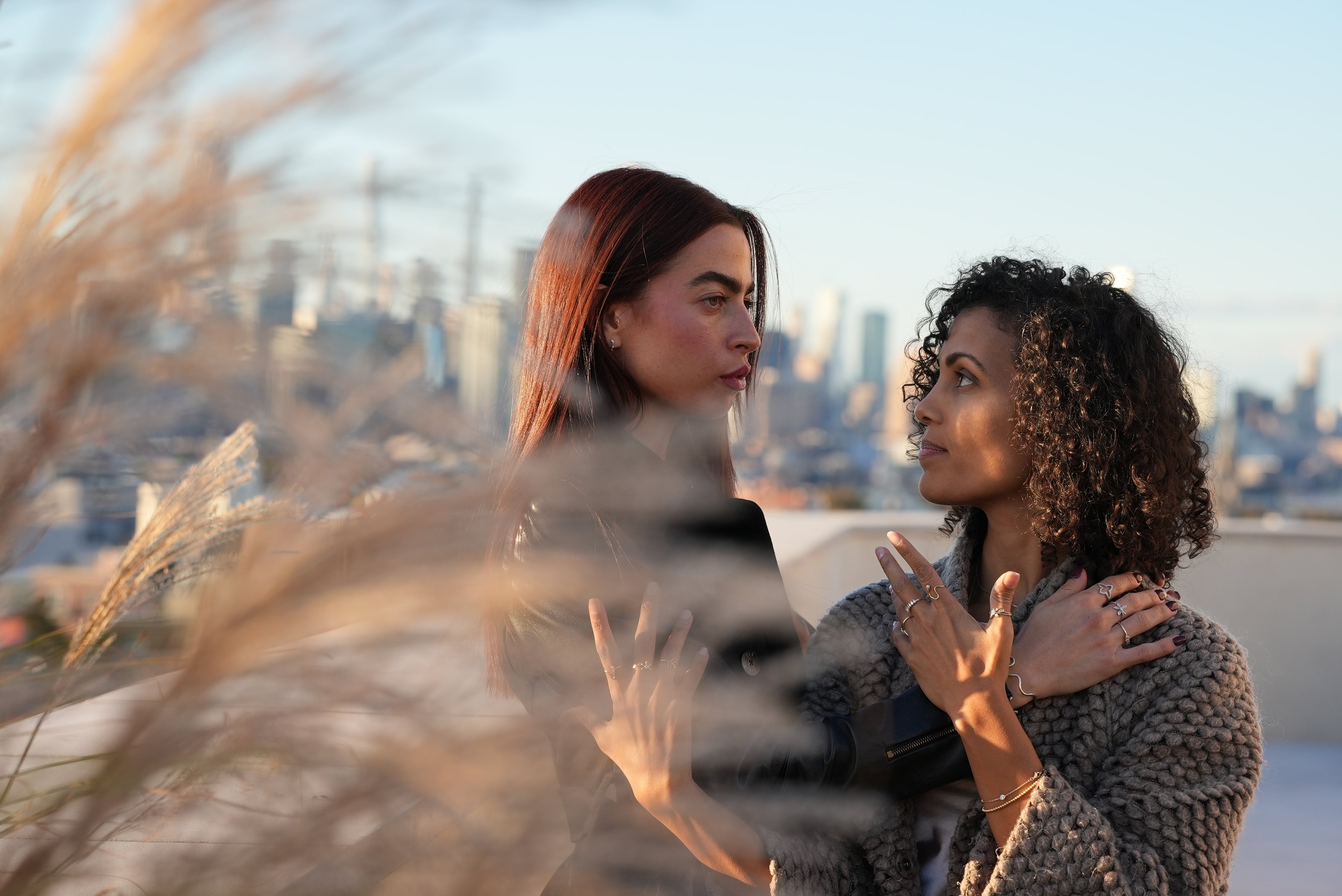 Two women embracing on a rooftop with a cityscape in the background