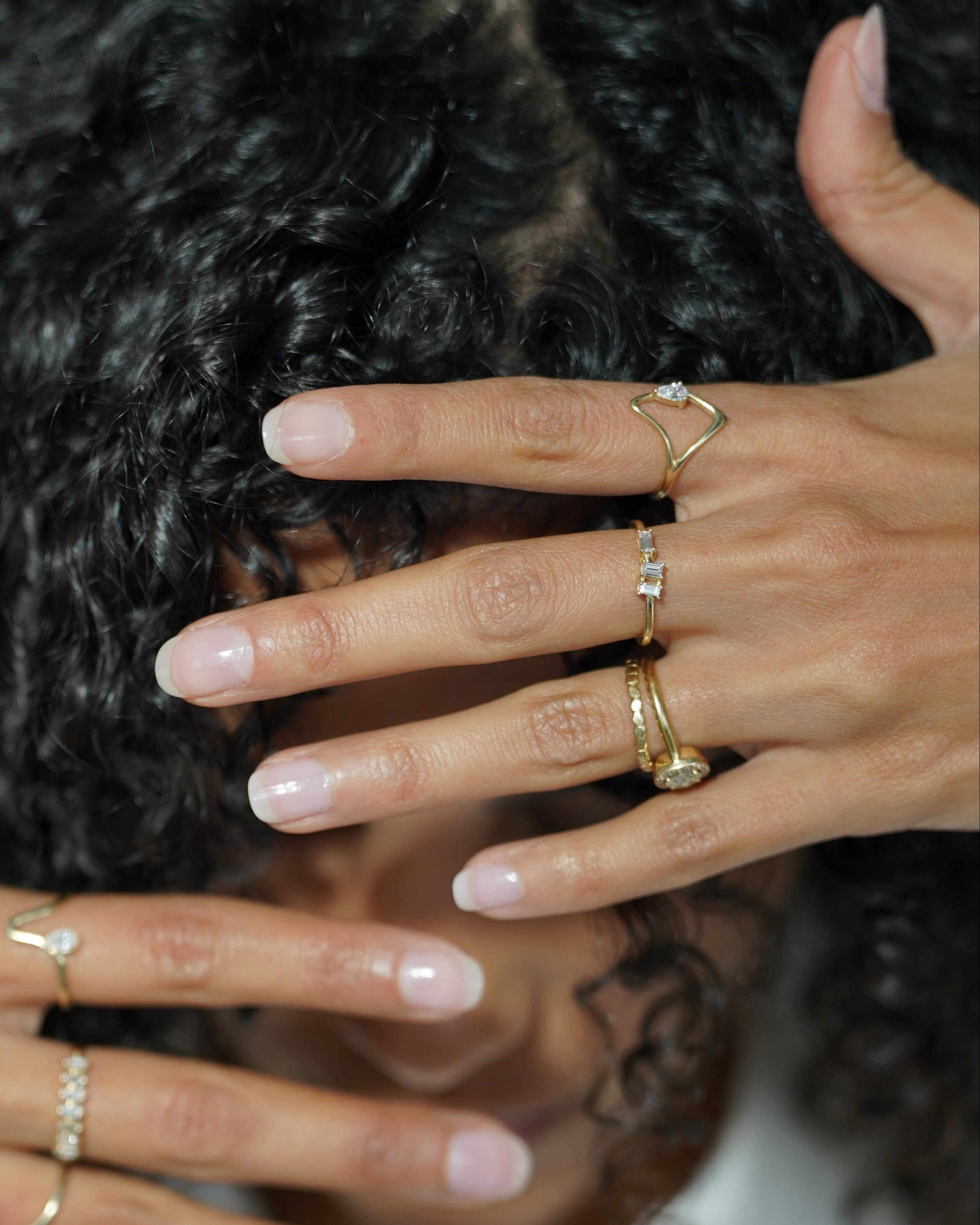 Person with multiple gold rings on fingers, partially covering face
