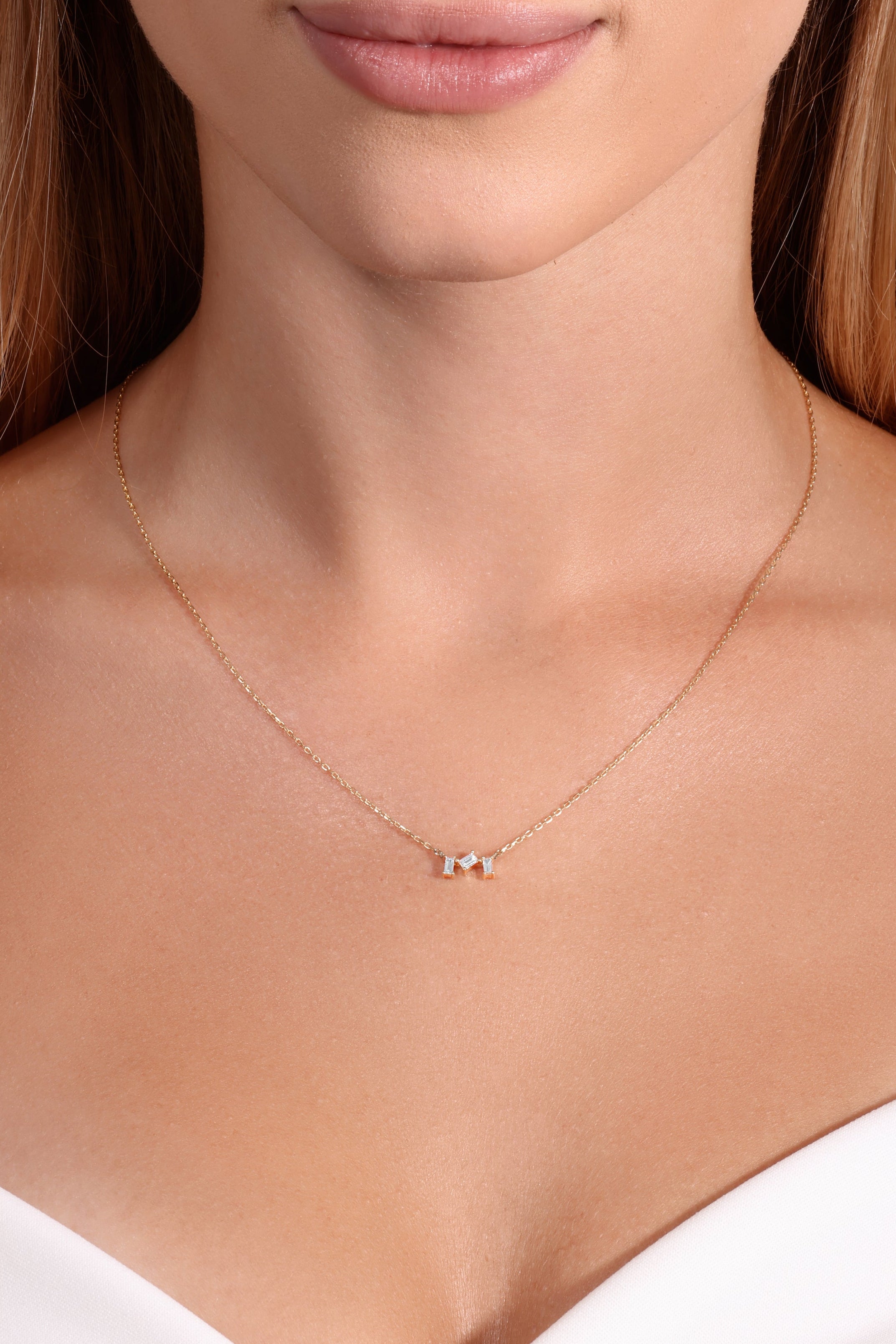 Necklace with small pendant on a person wearing a white top against a neutral background