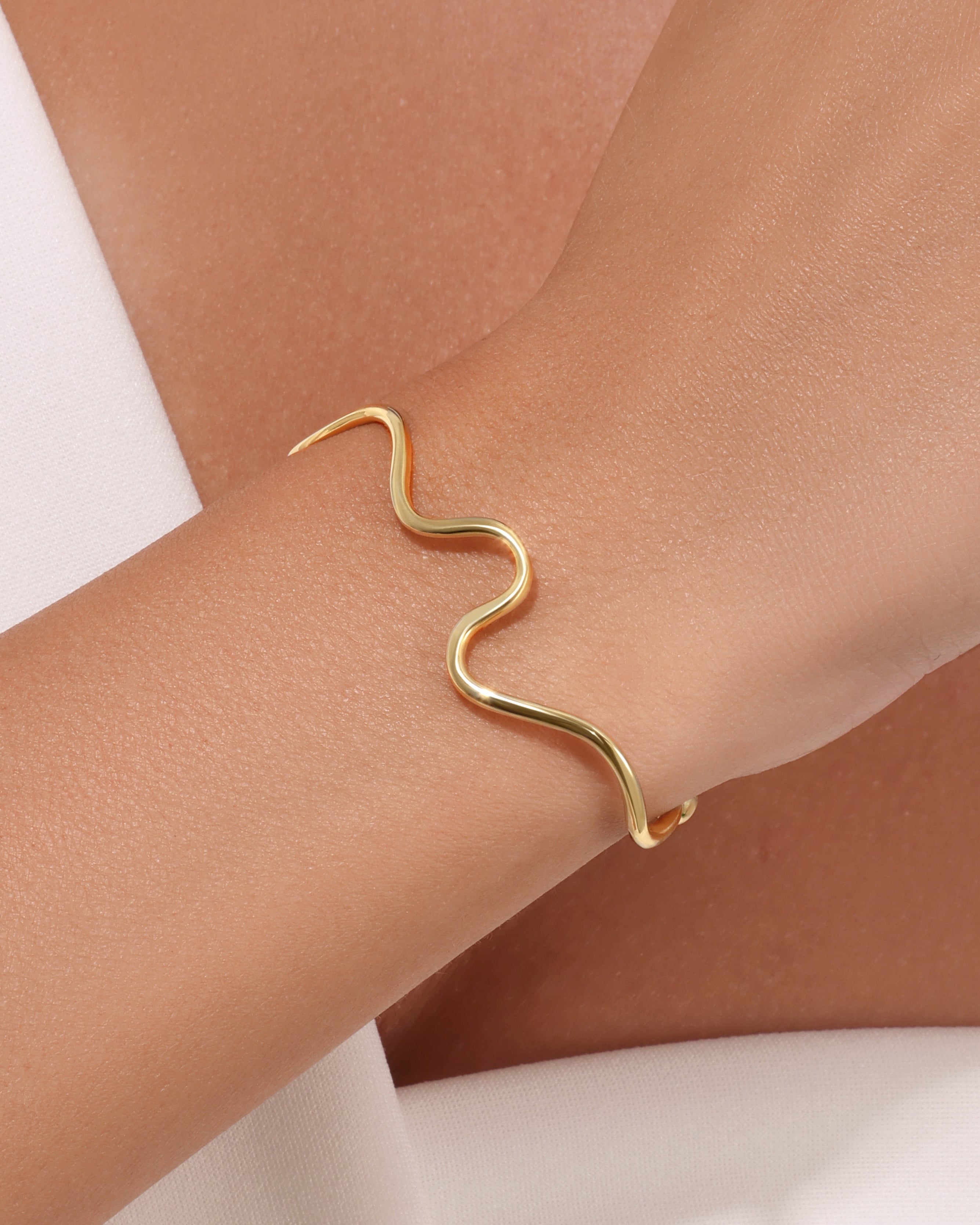 Gold bracelet on a wrist with a neutral background