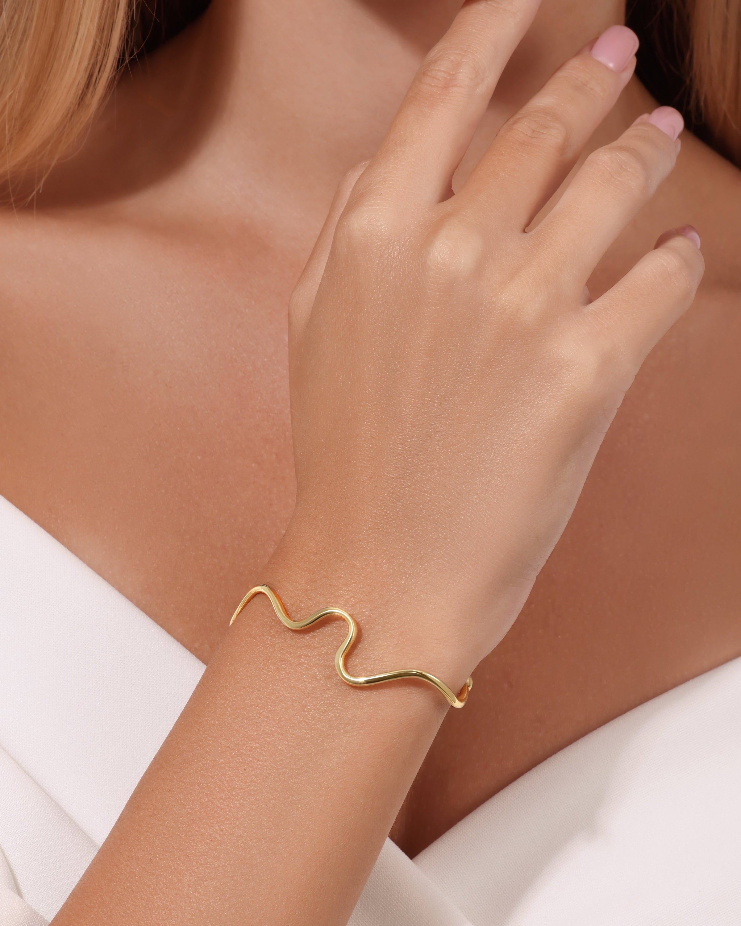 Gold bracelet on a wrist with a neutral background