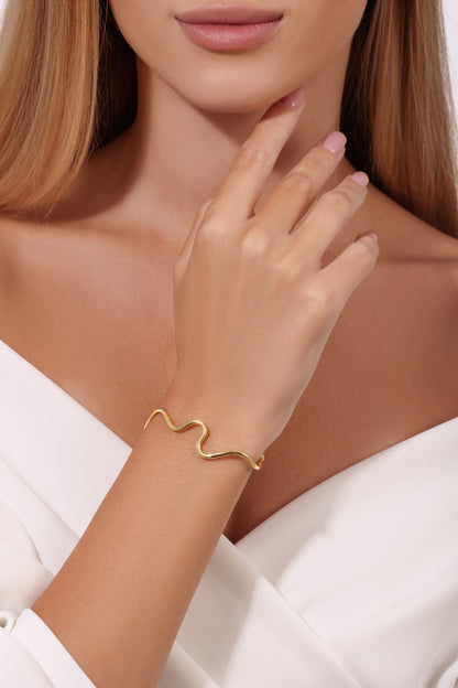 Gold bracelet on a wrist with a neutral background