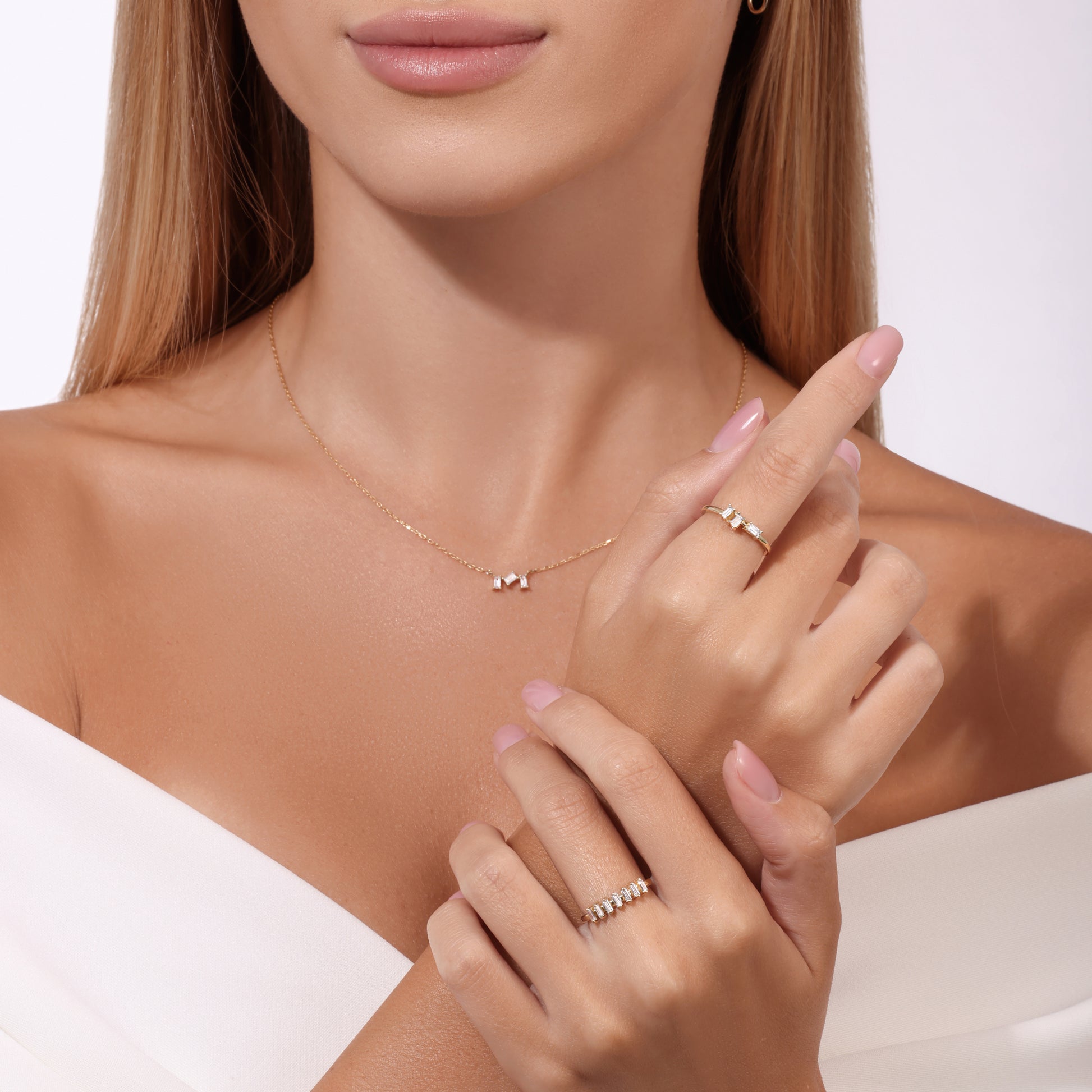 Model wearing 14k gold necklace with diamonds and two gold rings with baguette diamonds