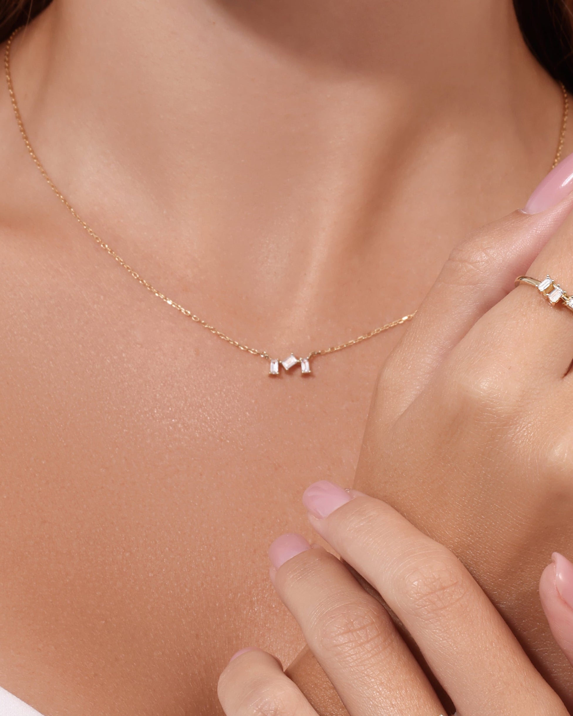 Gold necklace and rings on a model with a neutral background