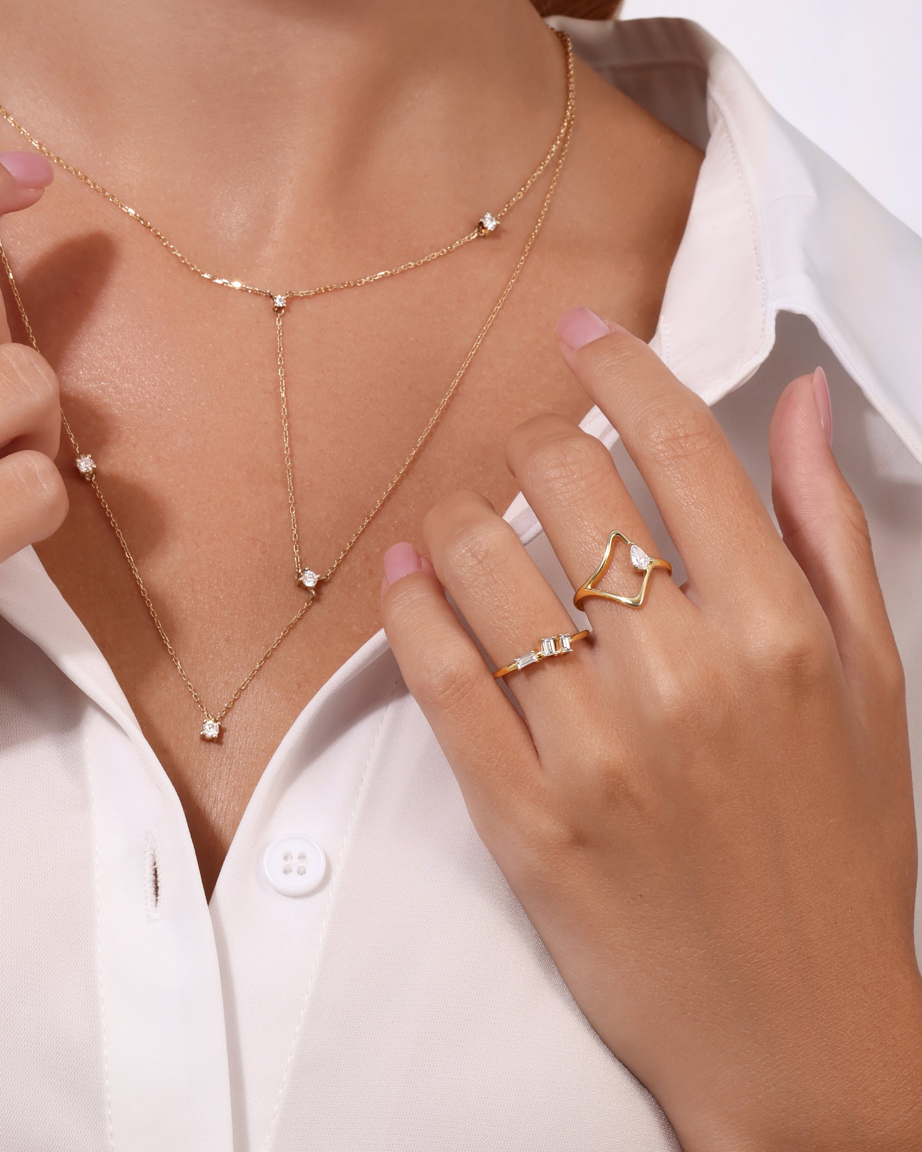 Close-up of a woman wearing a delicate gold necklace and ring on a white background