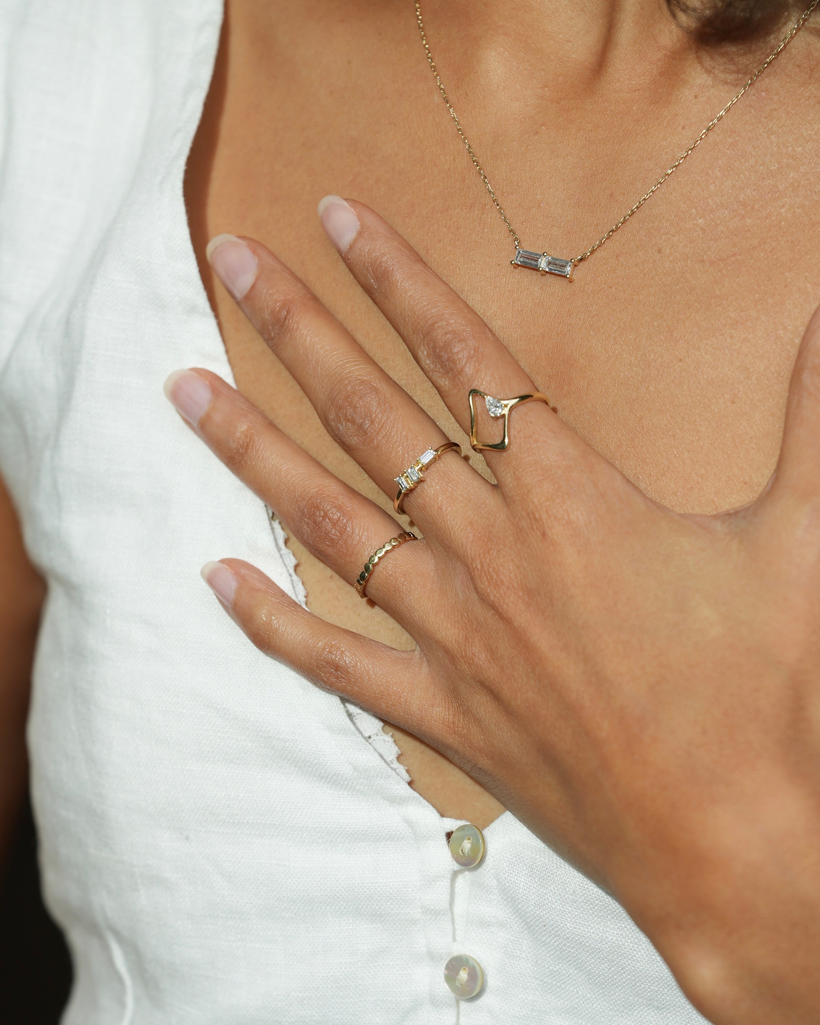 Close-up of a hand wearing gold rings with a blurred white shirt background
