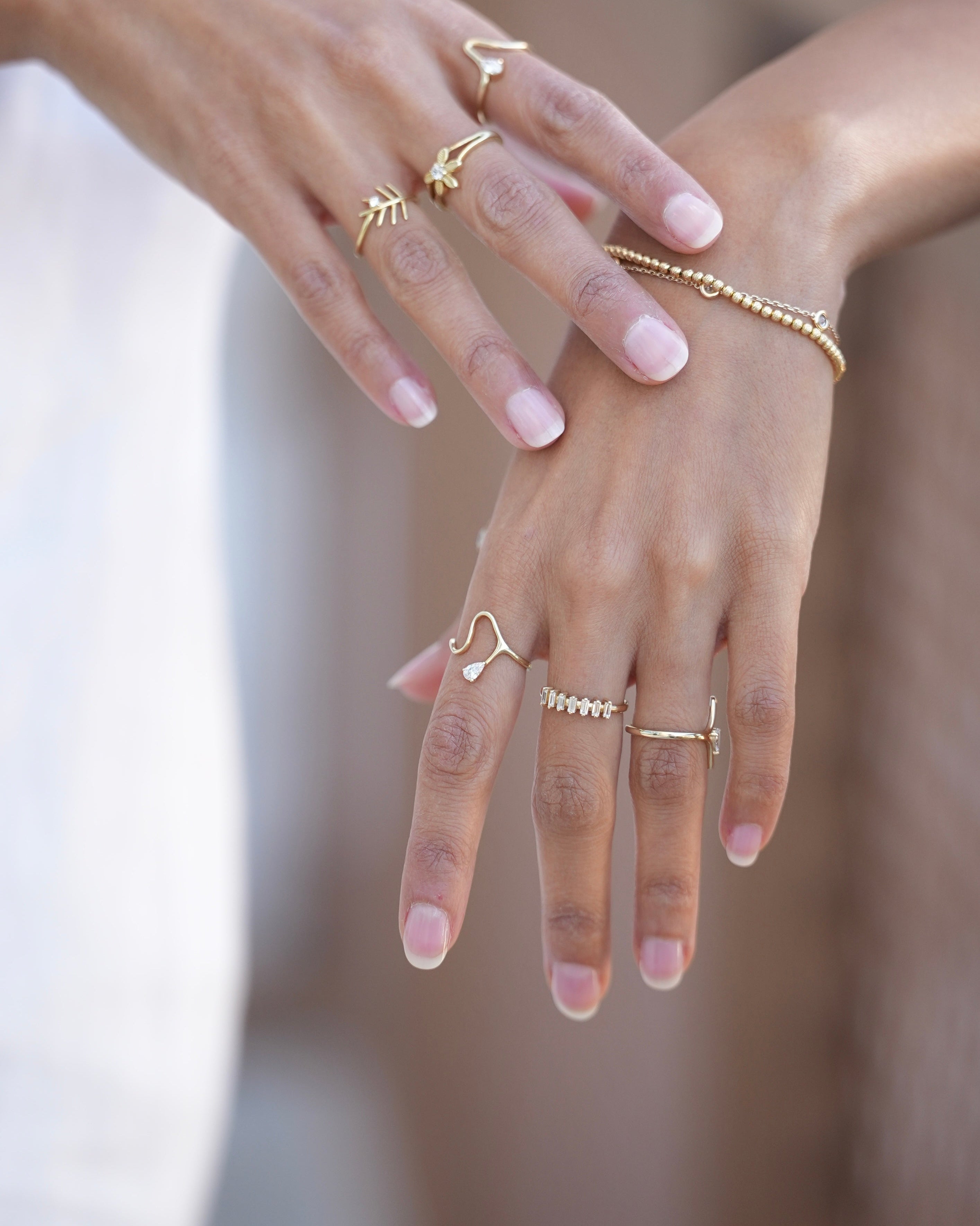 Close-up of hands wearing multiple gold rings on a blurred background