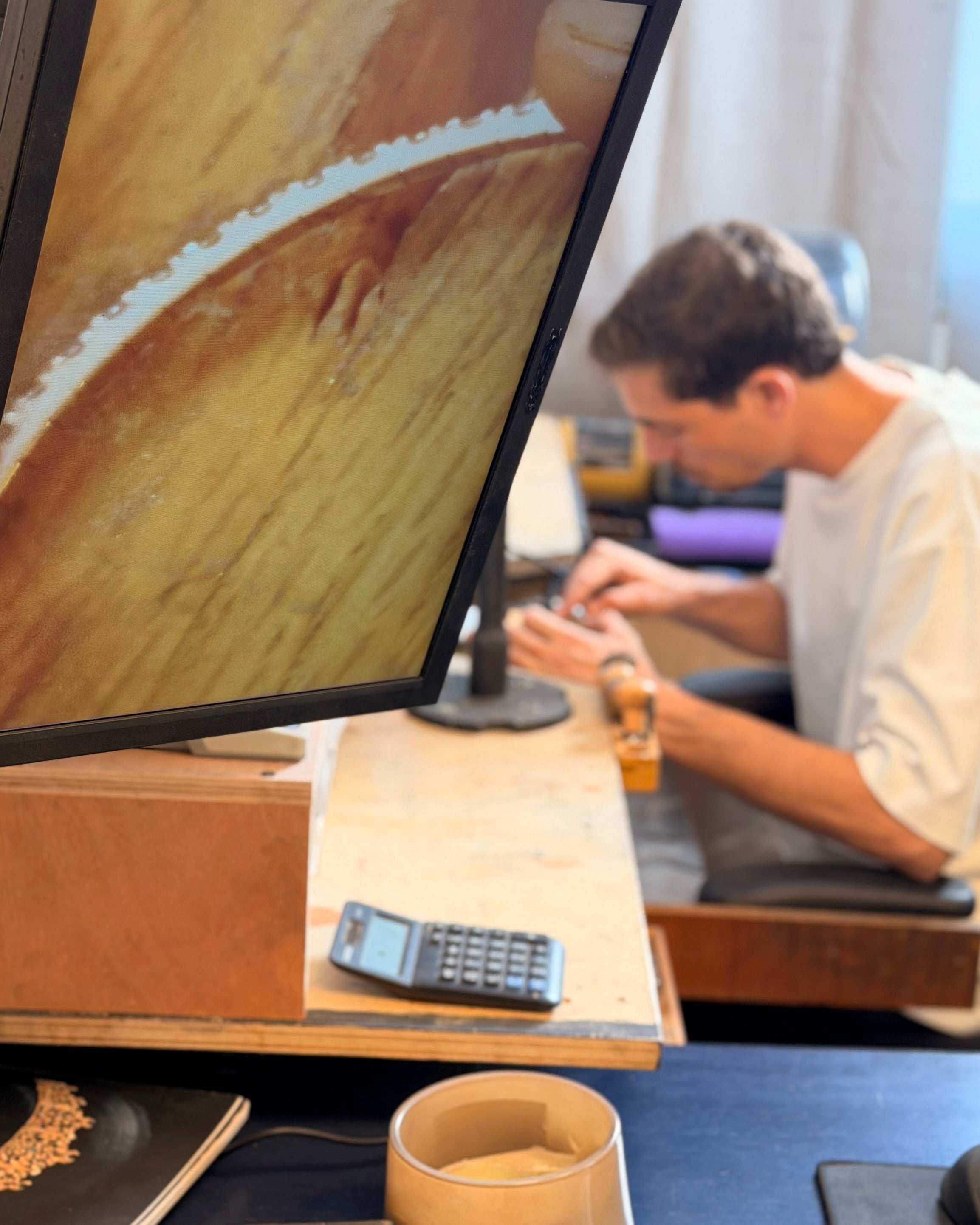 Person using a smartphone at a desk with a computer screen displaying a wooden surface.