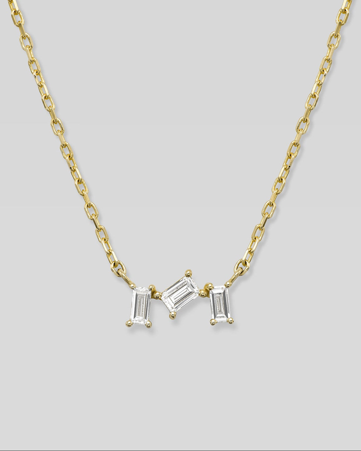 Gold necklace with three baguette-shaped diamonds on a light gray background