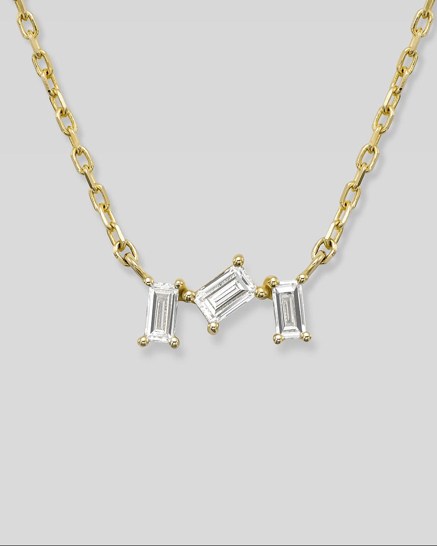 Gold necklace with three baguette-cut diamonds on a light gray background