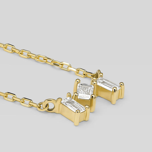 Gold necklace with three diamond pendants on a light gray background
