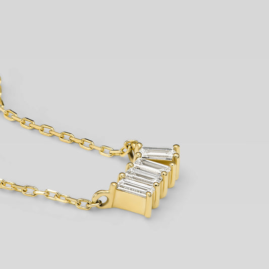 Gold necklace with four baguette-cut diamonds on a light gray background