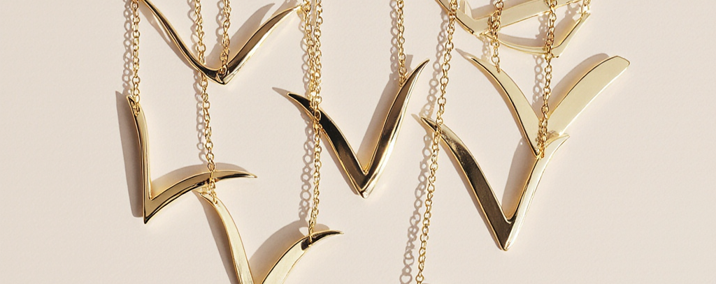 Gold necklaces with V-shaped pendants on a beige background